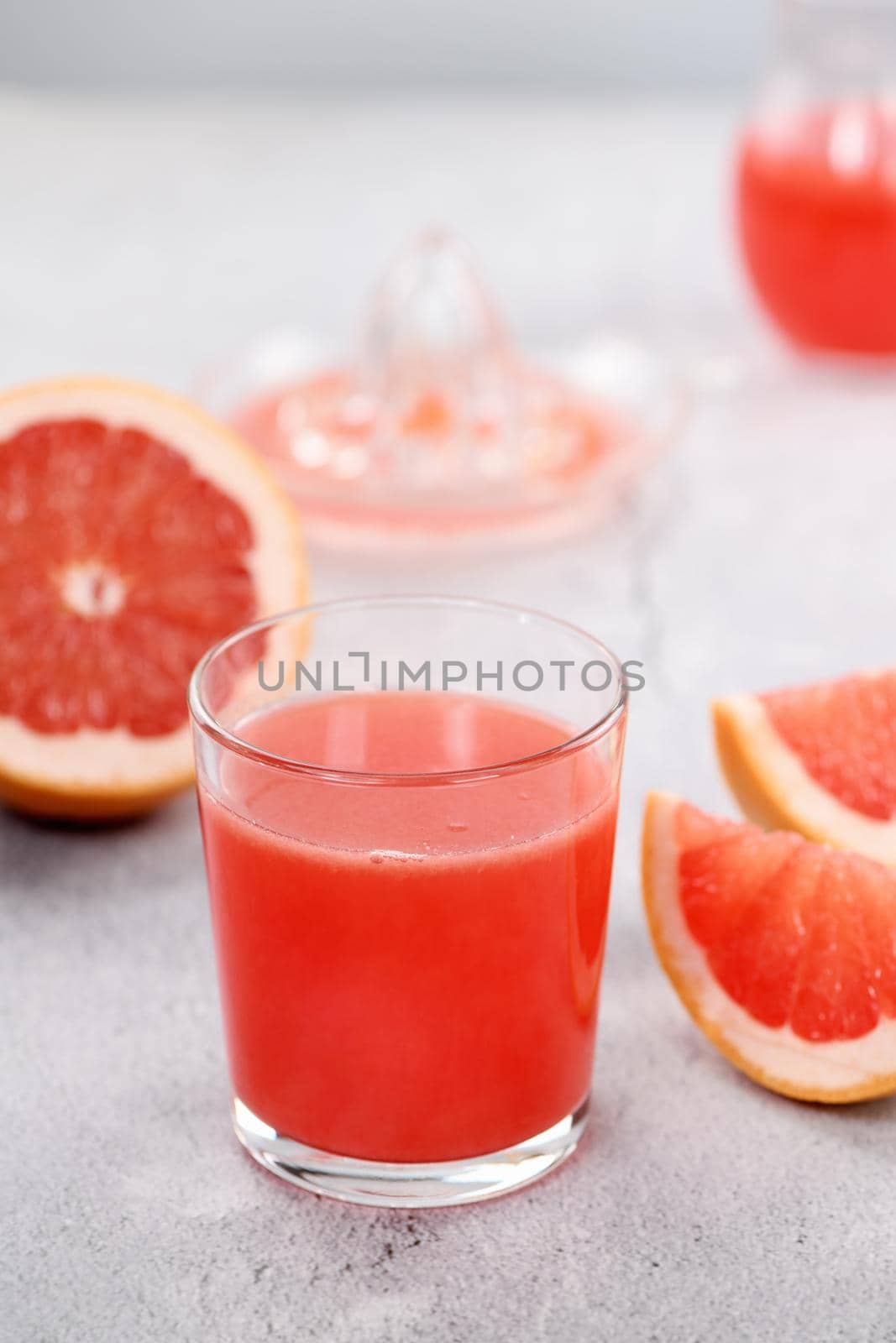 A glass of freshly made grapefruit juice and slices of fresh fruit on a light concrete background. Healthy and diet drink. Close-up