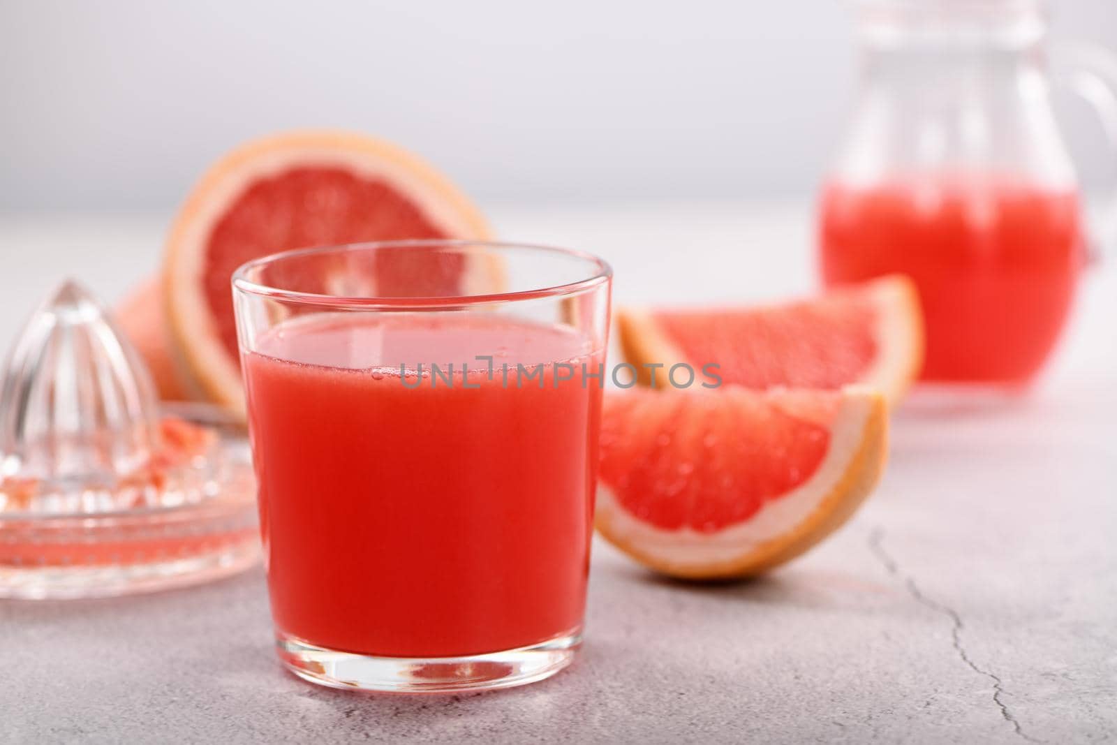 A glass of freshly made grapefruit juice and slices of fresh fruit on a light concrete background. Healthy and diet drink. Close-up