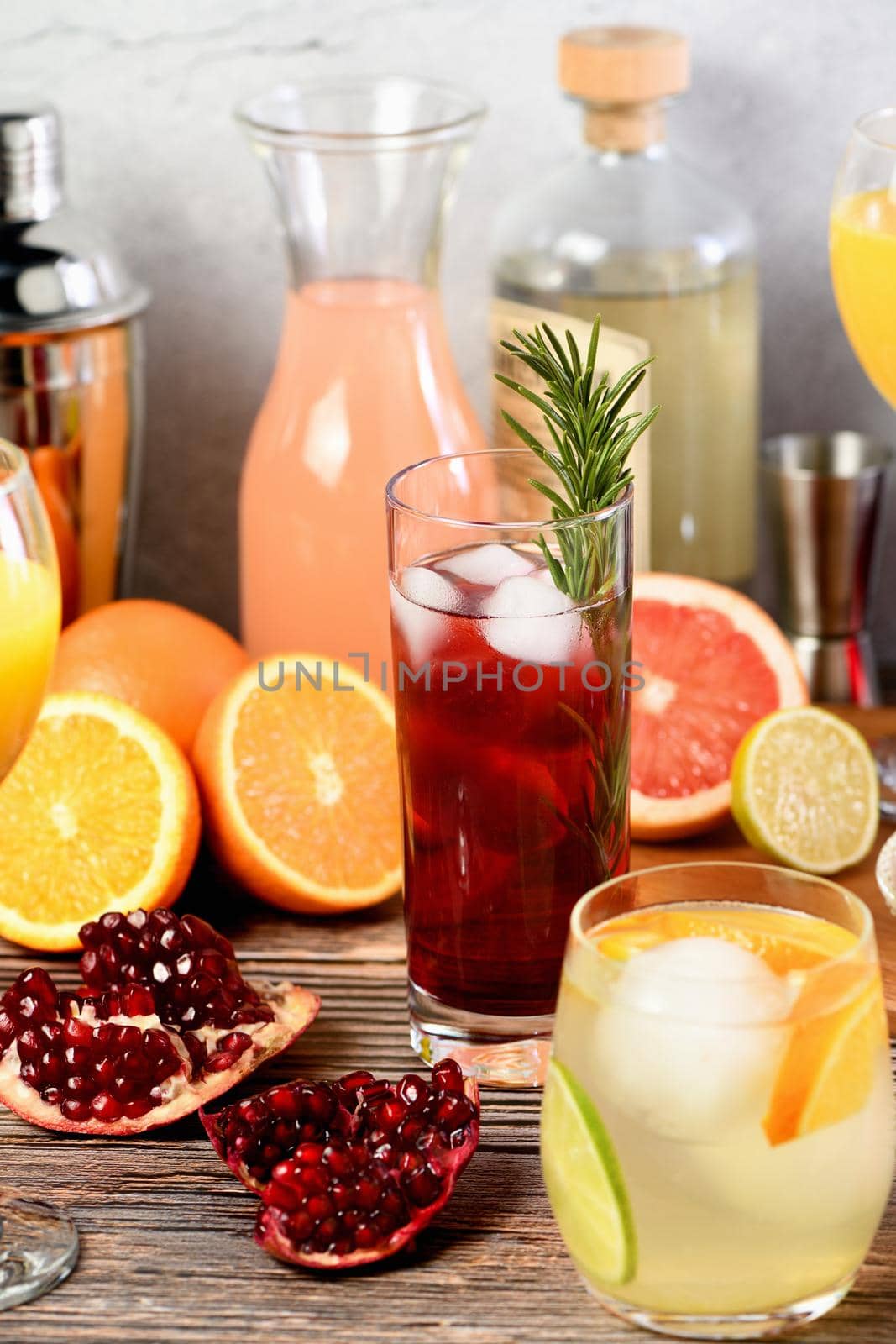 Gin cocktail with rosemary and pomegranate on a table among citrus fruits and drinks.