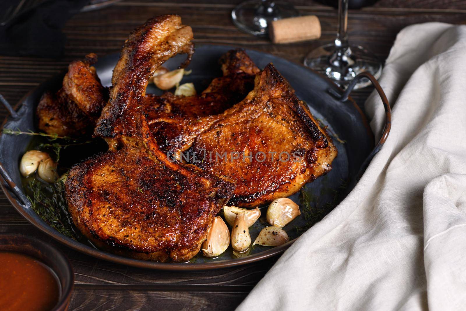 Juicy, slice of fried pork chop on a bone in oil with garlic and herbs in a pan. Close-up.