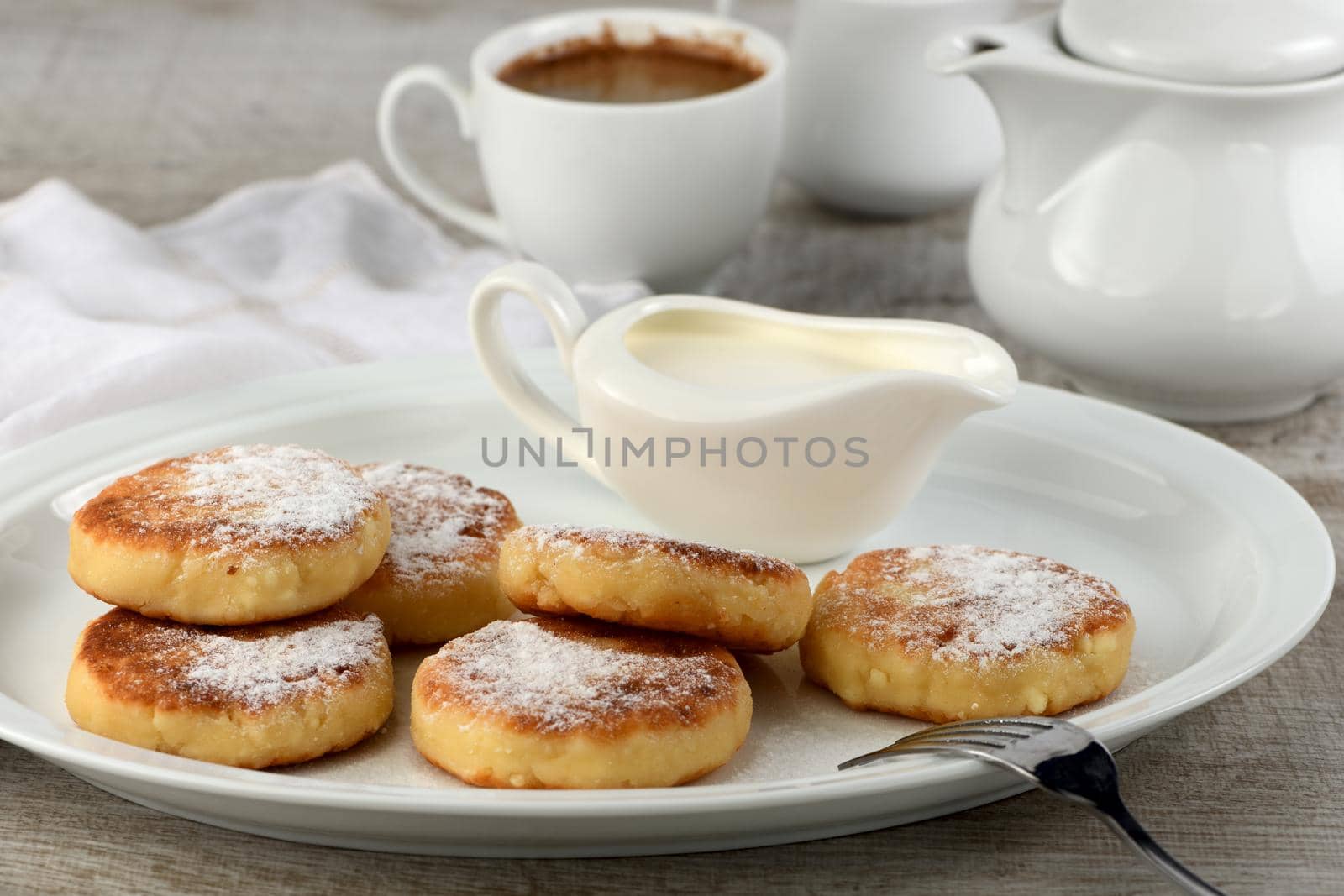 Breakfast. Cheese pancakes with sour cream sprinkled with powdered sugar on a white plate.