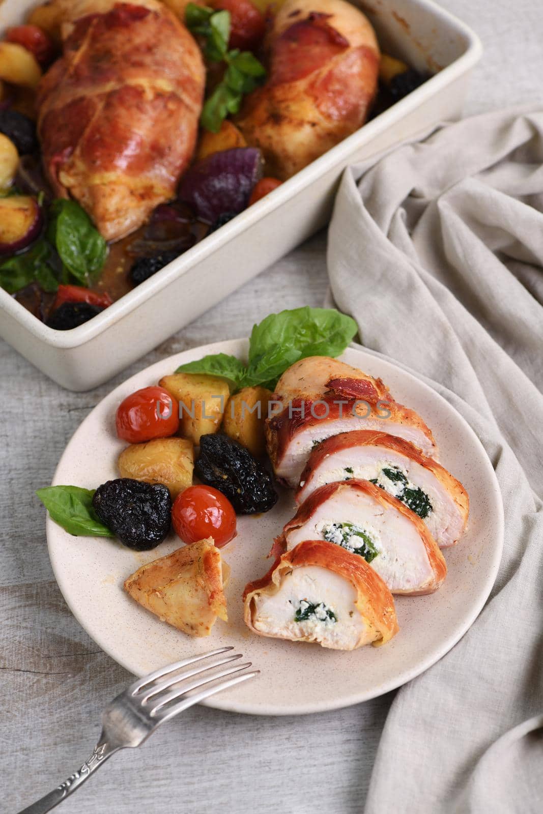 Sliced ​​chicken breast stuffed with goat cheese with spinach, wrapped in prosciutto, with a side dish of baked potatoes, tomato and dried prunes