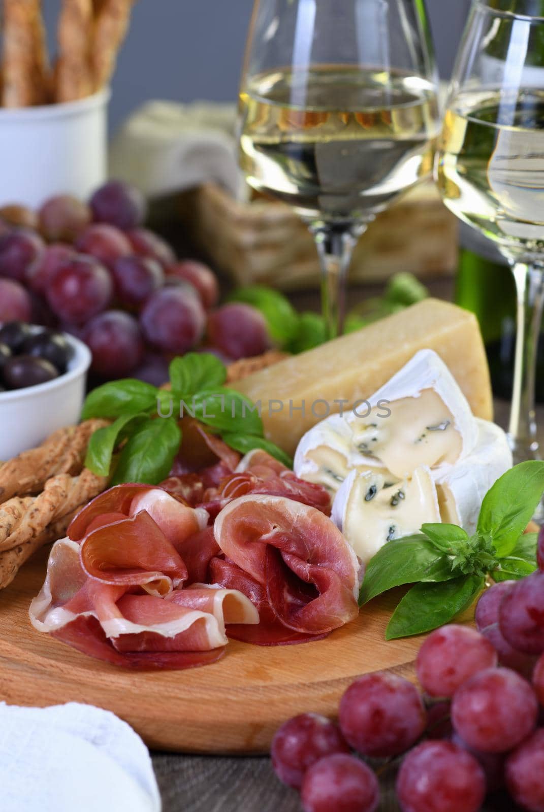 Antipasto. Wine set snacks of dried ham, camembert cheese with mold, parmesan with grissini, olives and pink grapes.