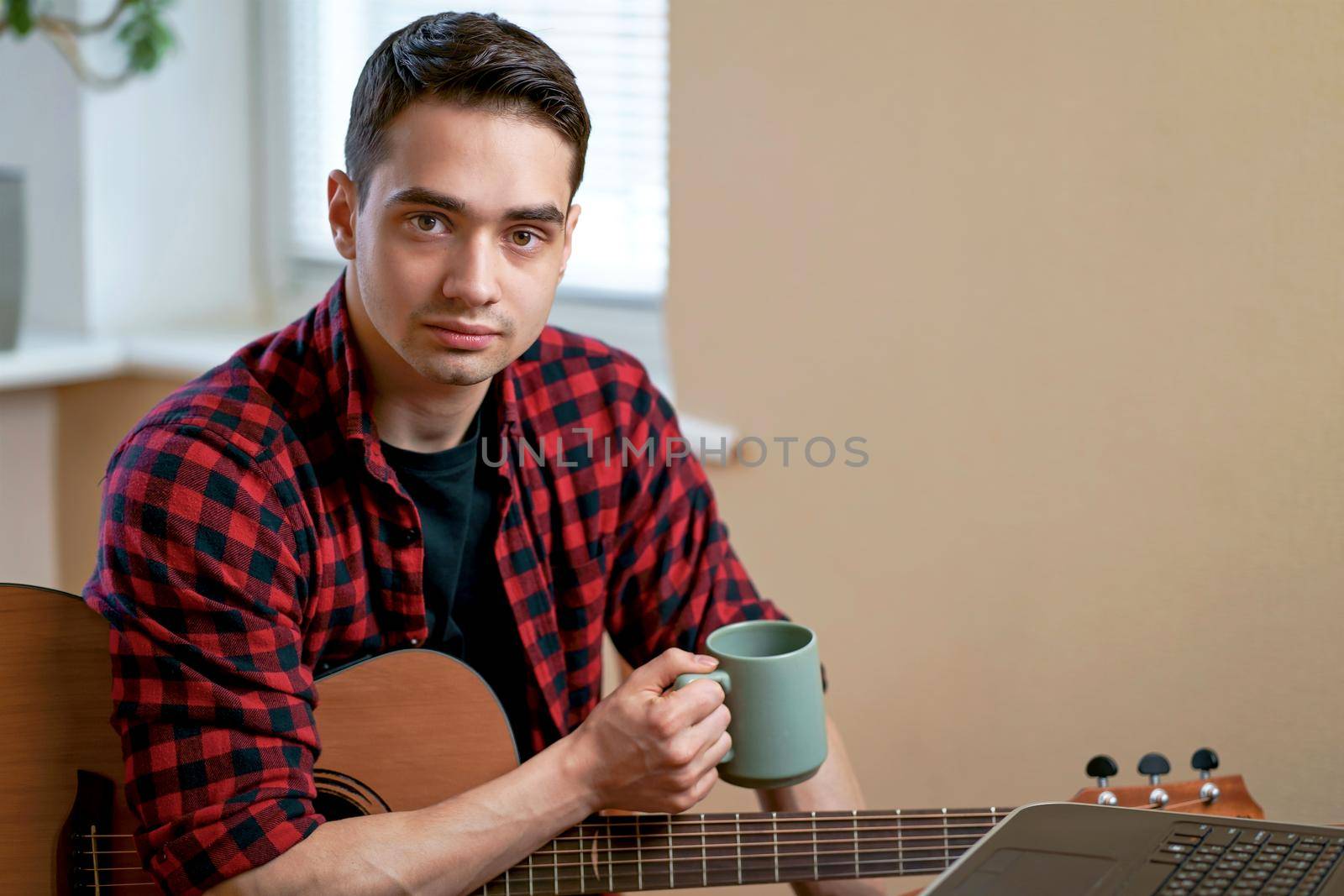 A young man learns to play the guitar using the Internet, laptop, online lesson. Hobby and leisure concept by aprilphoto