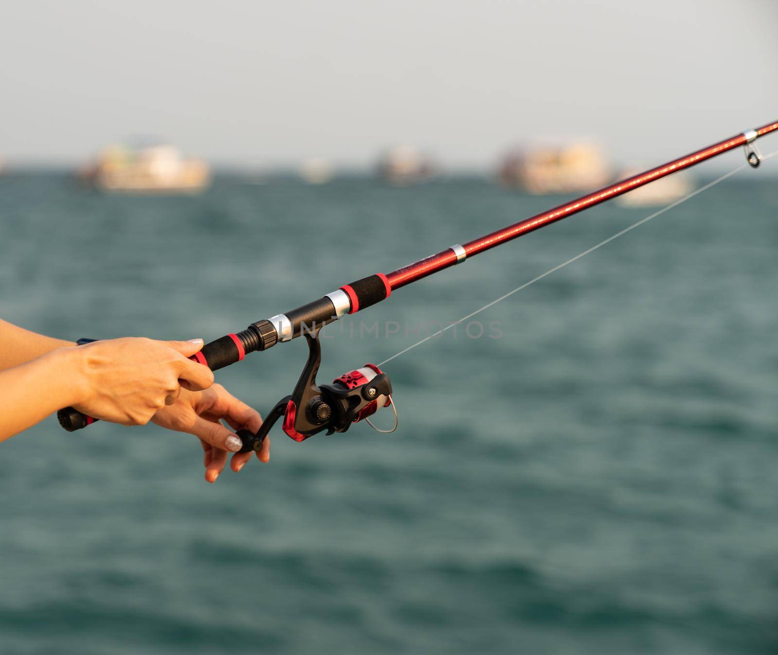 Woman hand holding fishing rod with sea background, fishing at sunset. by sirawit99