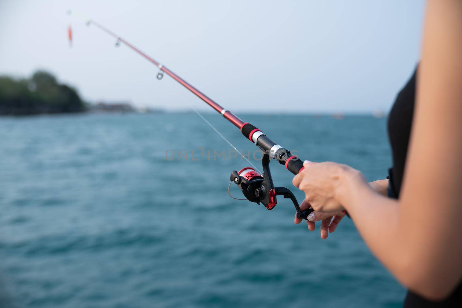 Woman hand holding fishing rod with sea background, fishing at sunset.