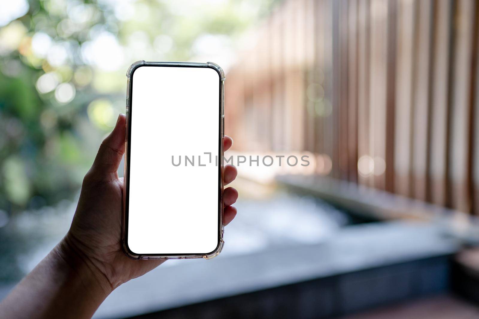 Hands holding white mobile phone with blank screen mock up, hotel spa background. by sirawit99