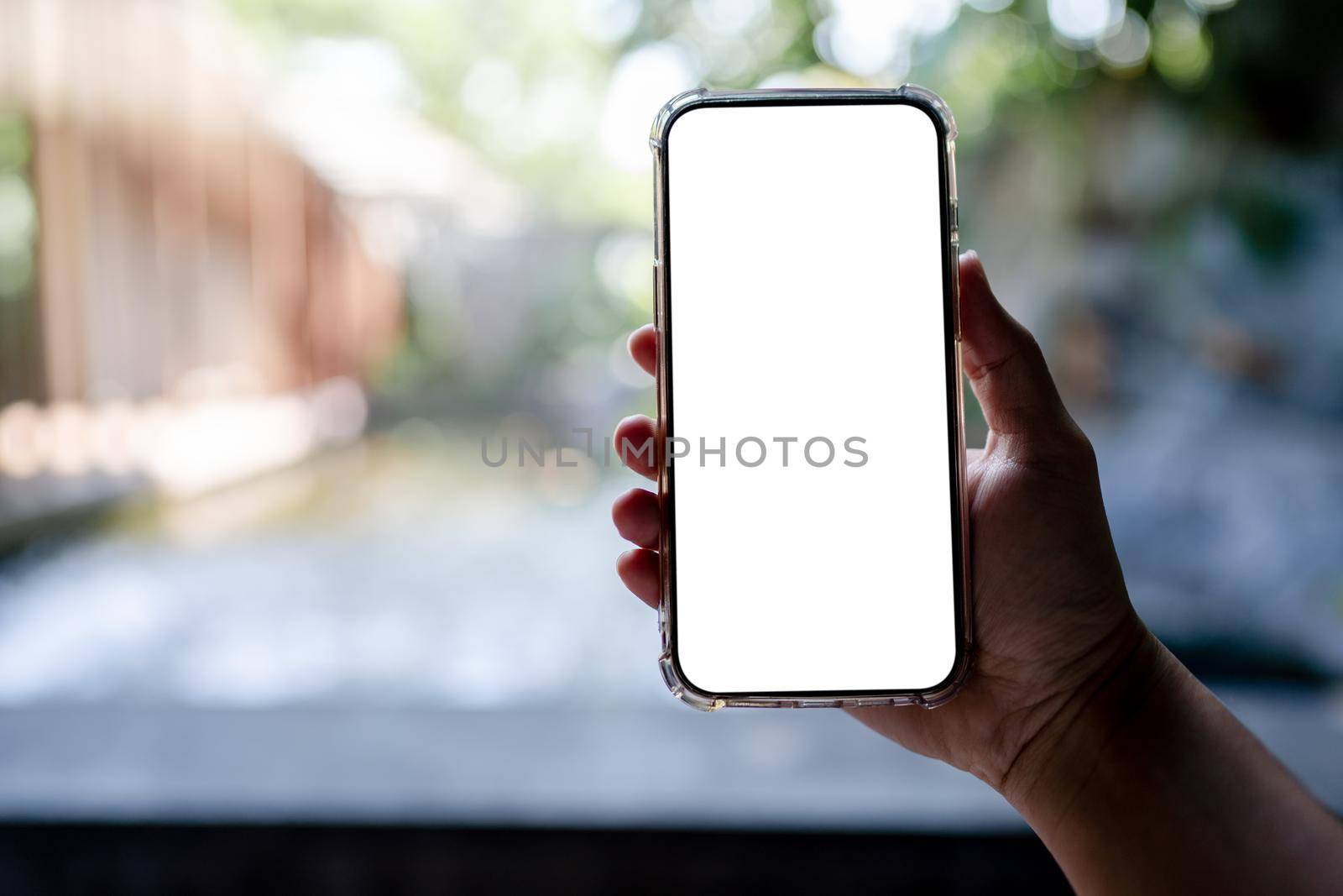 Hands holding white mobile phone with blank screen mock up, hotel spa background.