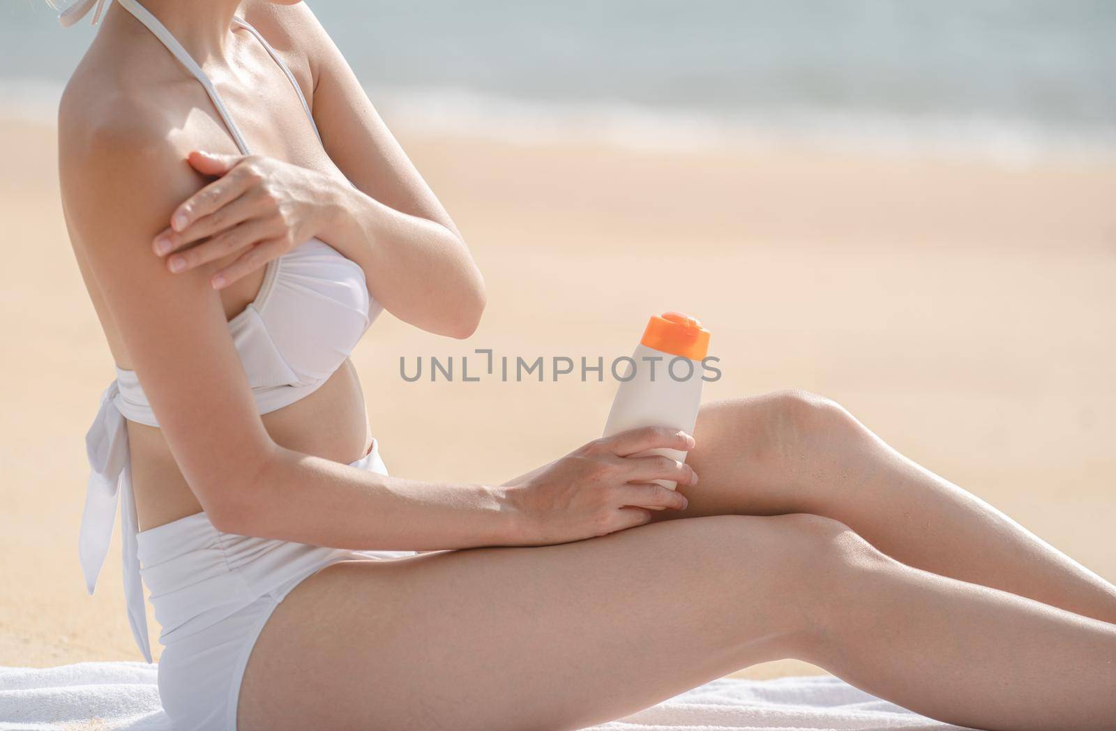Woman on the beach applying Sunscreen while sitting on towel.