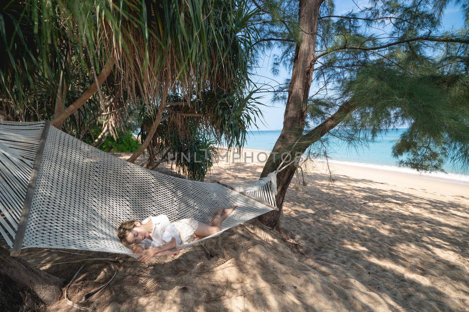 Woman lying in a hammock under the tree shadow on a beach.