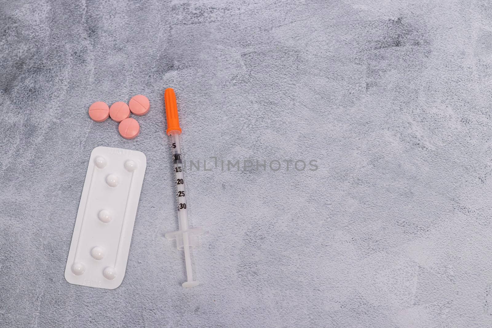 A blister pack of pills and a syringe on a marbled gray background