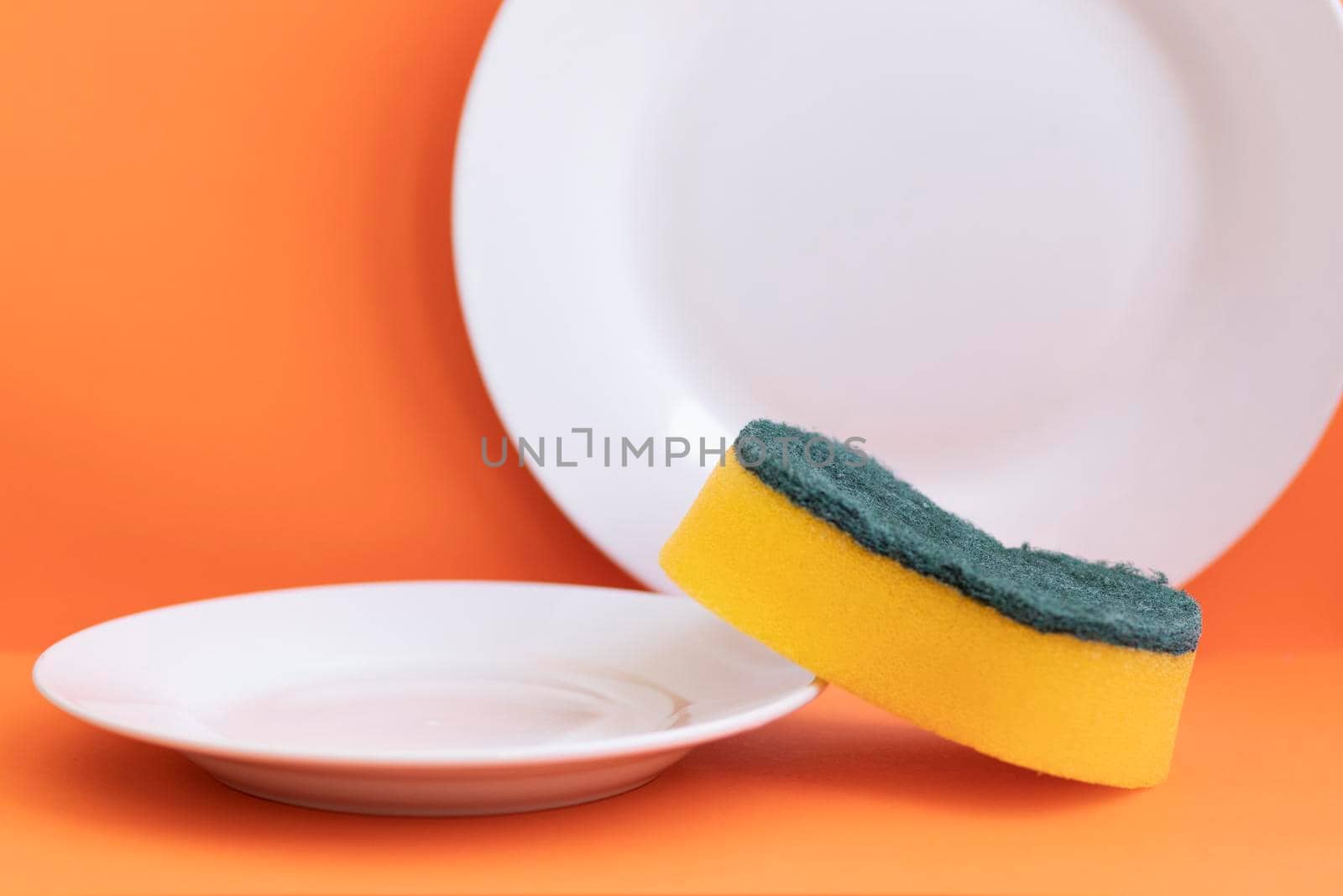 Yellow sponge next to white plate with orange background
