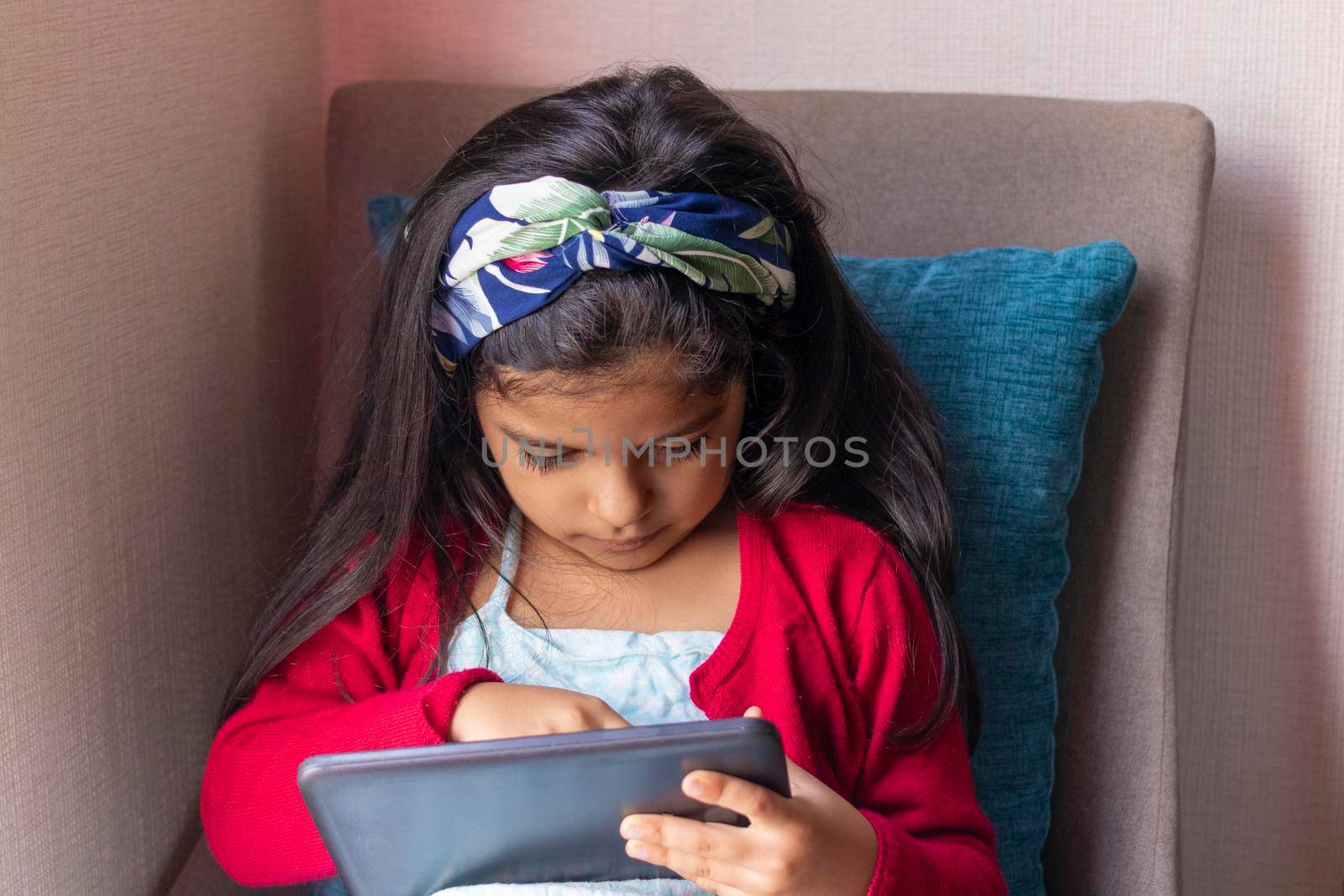 Little girl sitting is playing with her tablet at home