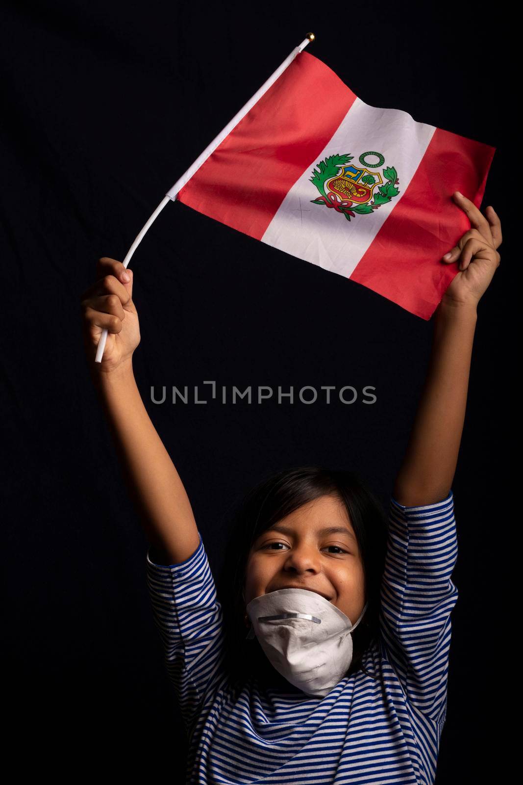 Portrait of little Peruvian girl wearing medical mask and holding hopefully the flag of Peru