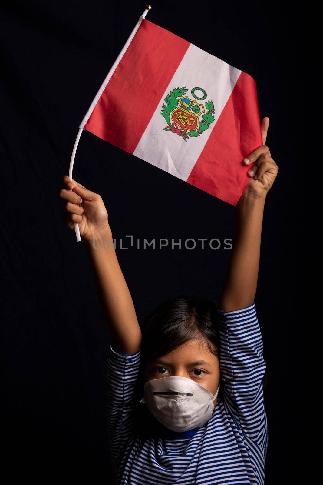 Portrait of little Peruvian girl wearing medical mask and holding hopefully the flag of Peru