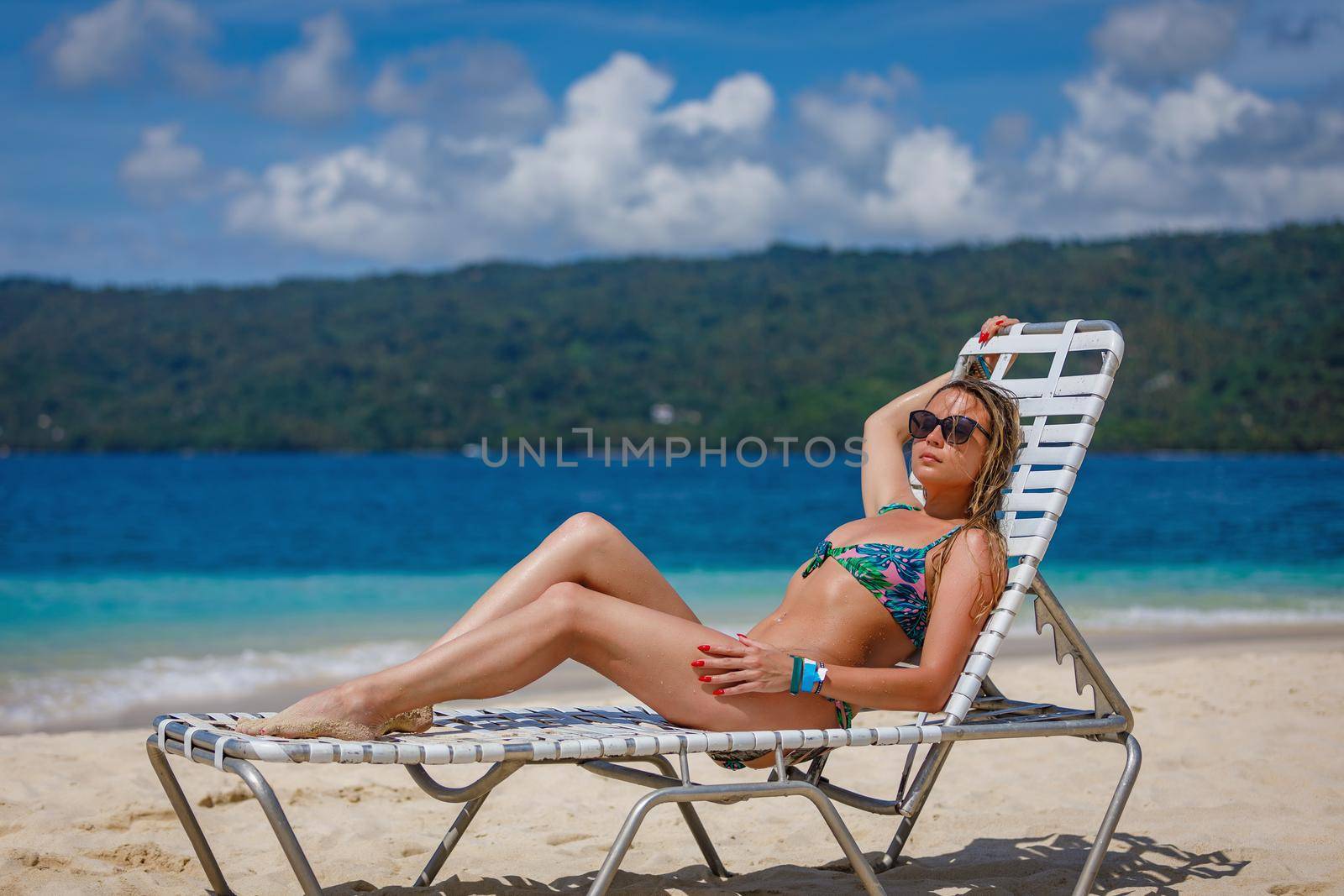 A young beautiful girl sunbathes on a sun lounger by the ocean. White sand, azure water