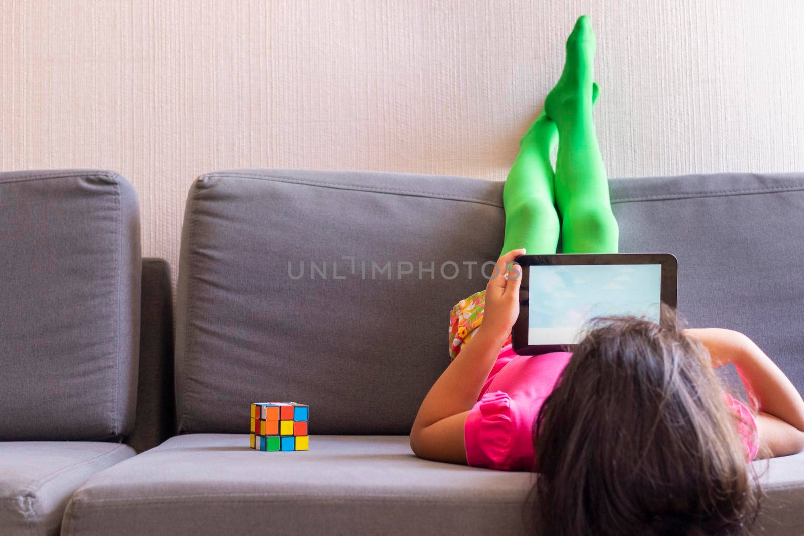 Little girl playing with her tablet lying on the sofa