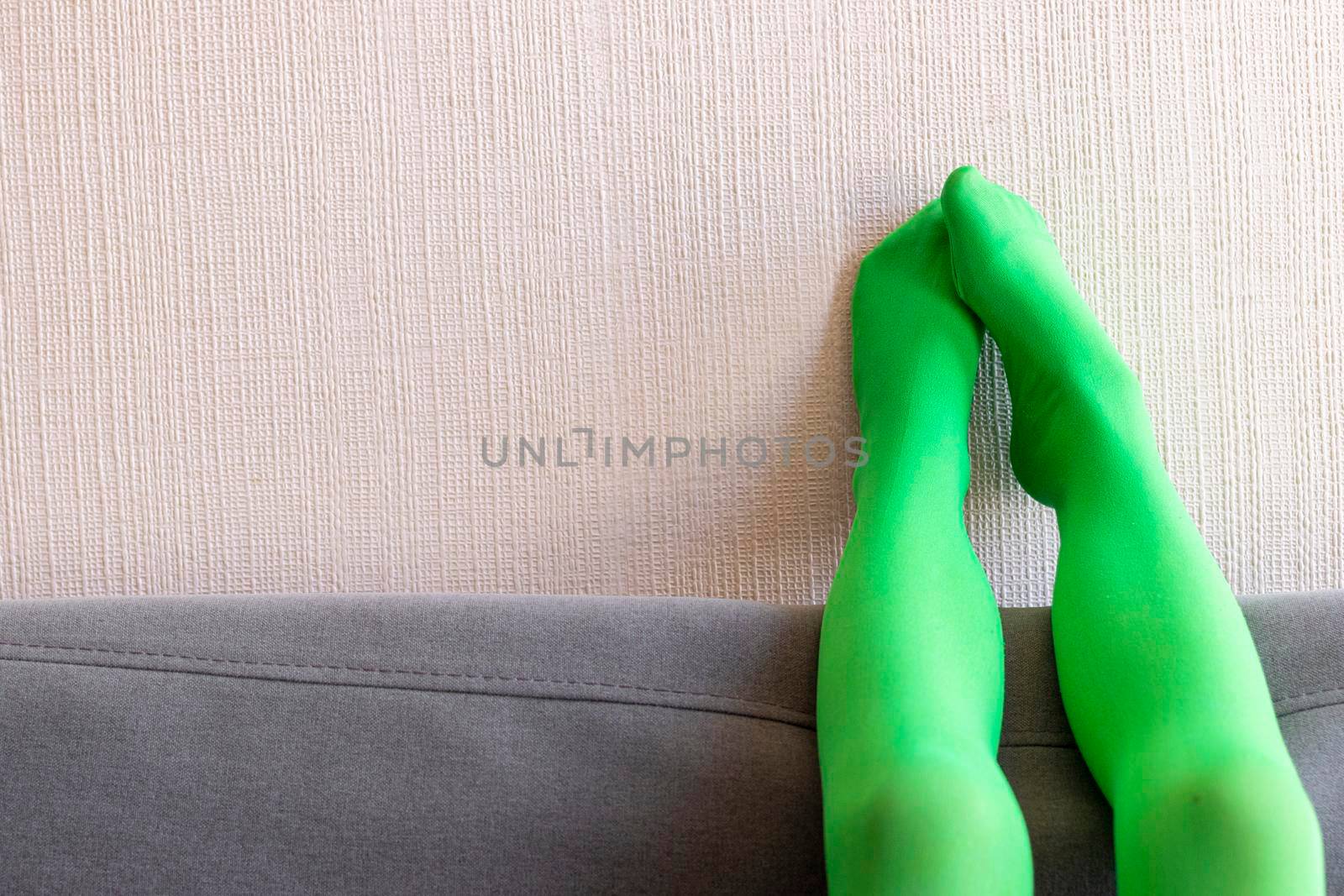 Legs up with green pantyhose resting on the wall and sofa