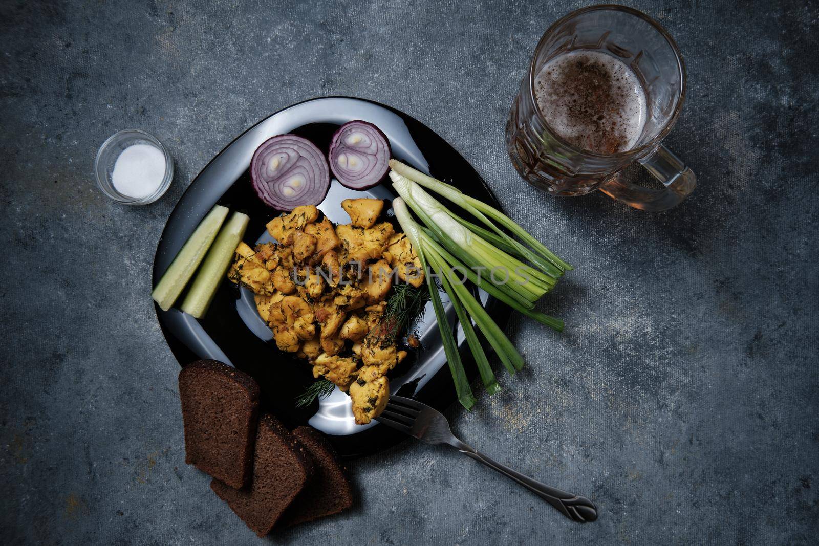 Chicken dish, black bread, onions and cucumbers on a dark background.