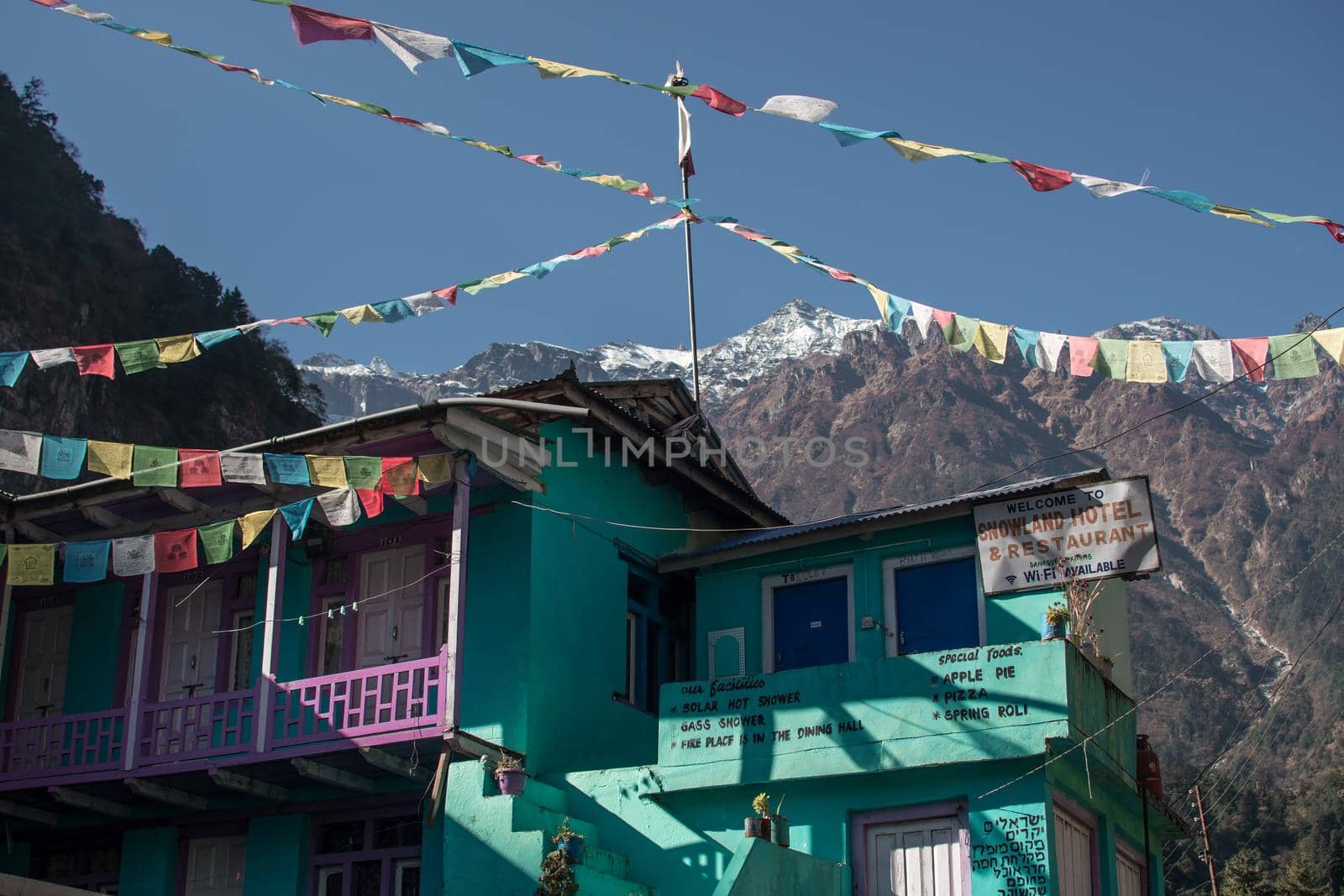Turquoise tea house with buddhist prayer flags underneath snow covered peak along Annapurna circuit, Himalaya, Nepal, Asia