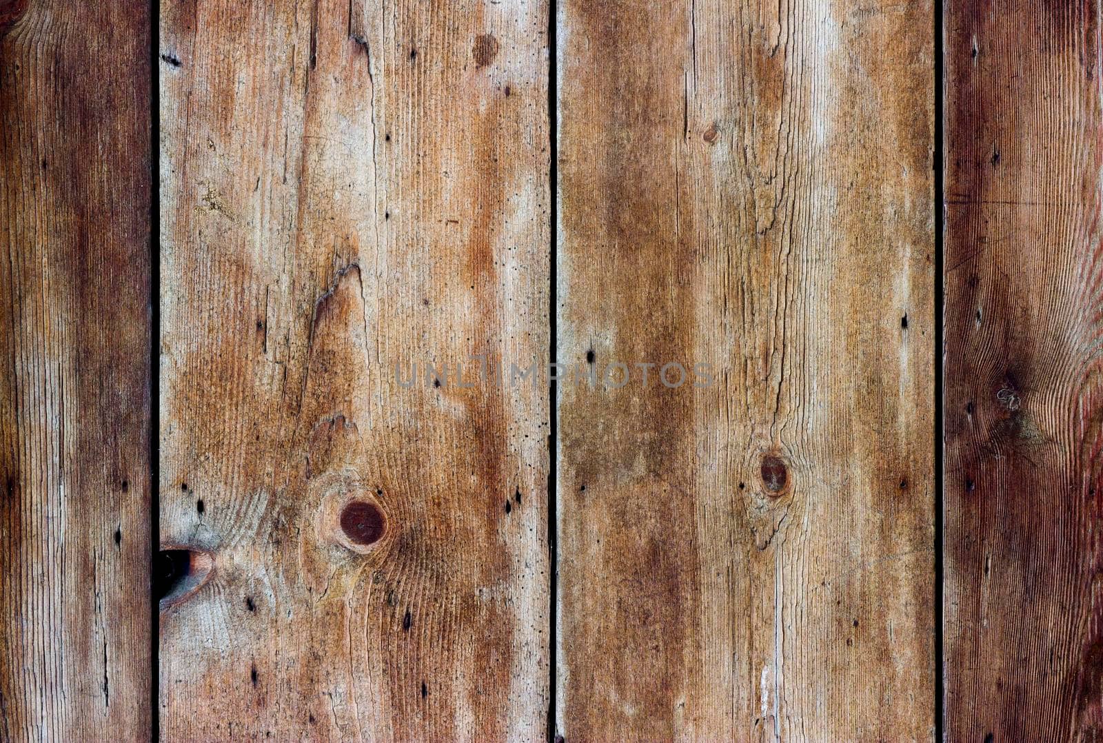 Boards of aged wood arranged vertically. The wood is weathered, heavily textured and coloured yellow, gold and brown.