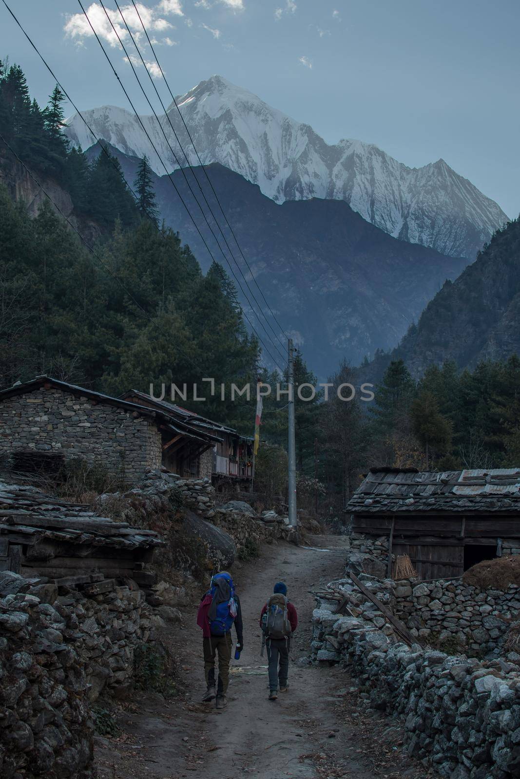 Two hikers trekking through nepalese mountain village by arvidnorberg