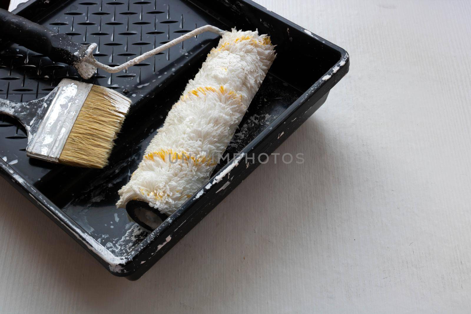 In a black tray on a white background are a brush and a roller for painting the walls. Repair concept.