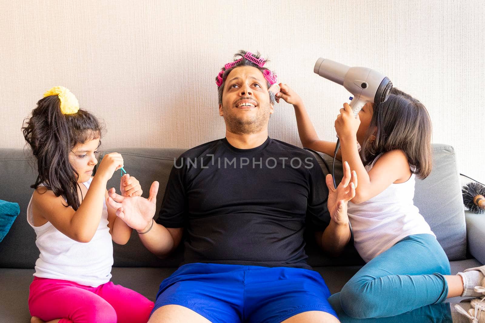 Pretty daughters are painting the nails and combing the hair of their handsome young father