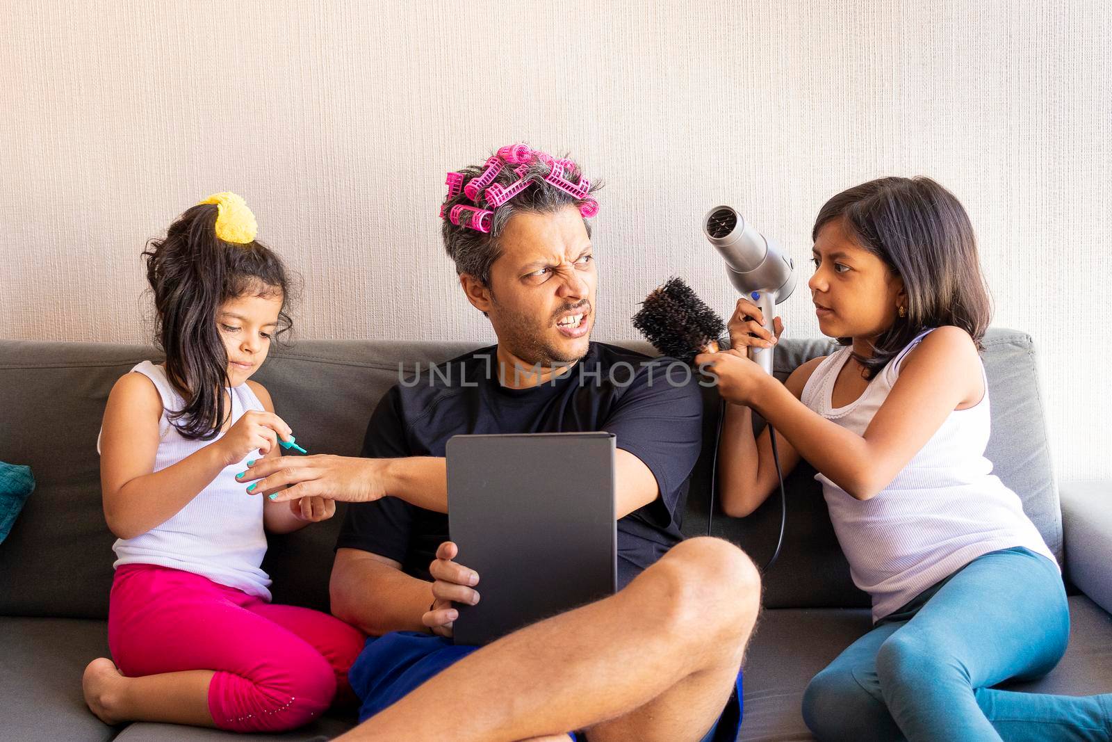 Pretty daughters are painting the nails and combing the hair of their handsome young father