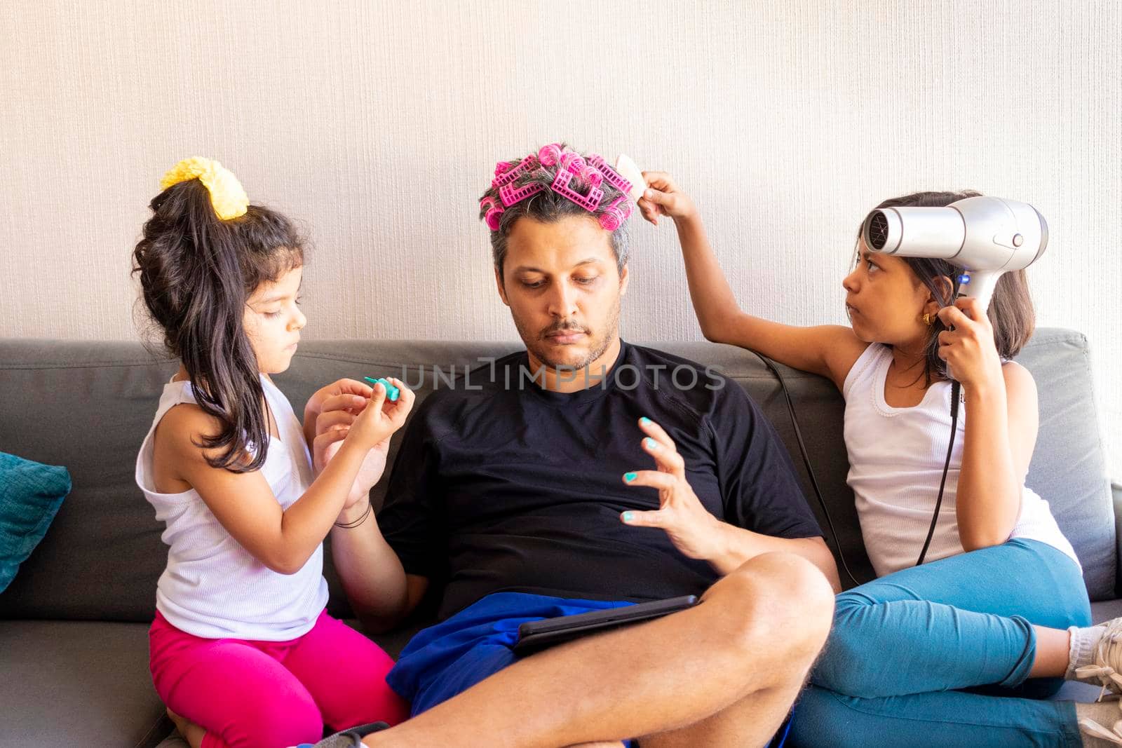 Pretty daughters are painting the nails and combing the hair of their handsome young father