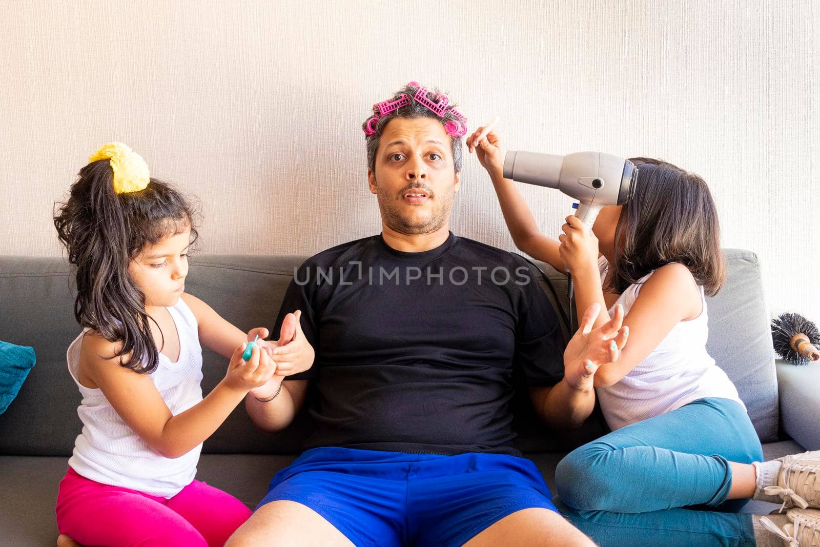 Pretty daughters are painting the nails and combing the hair of their handsome young father