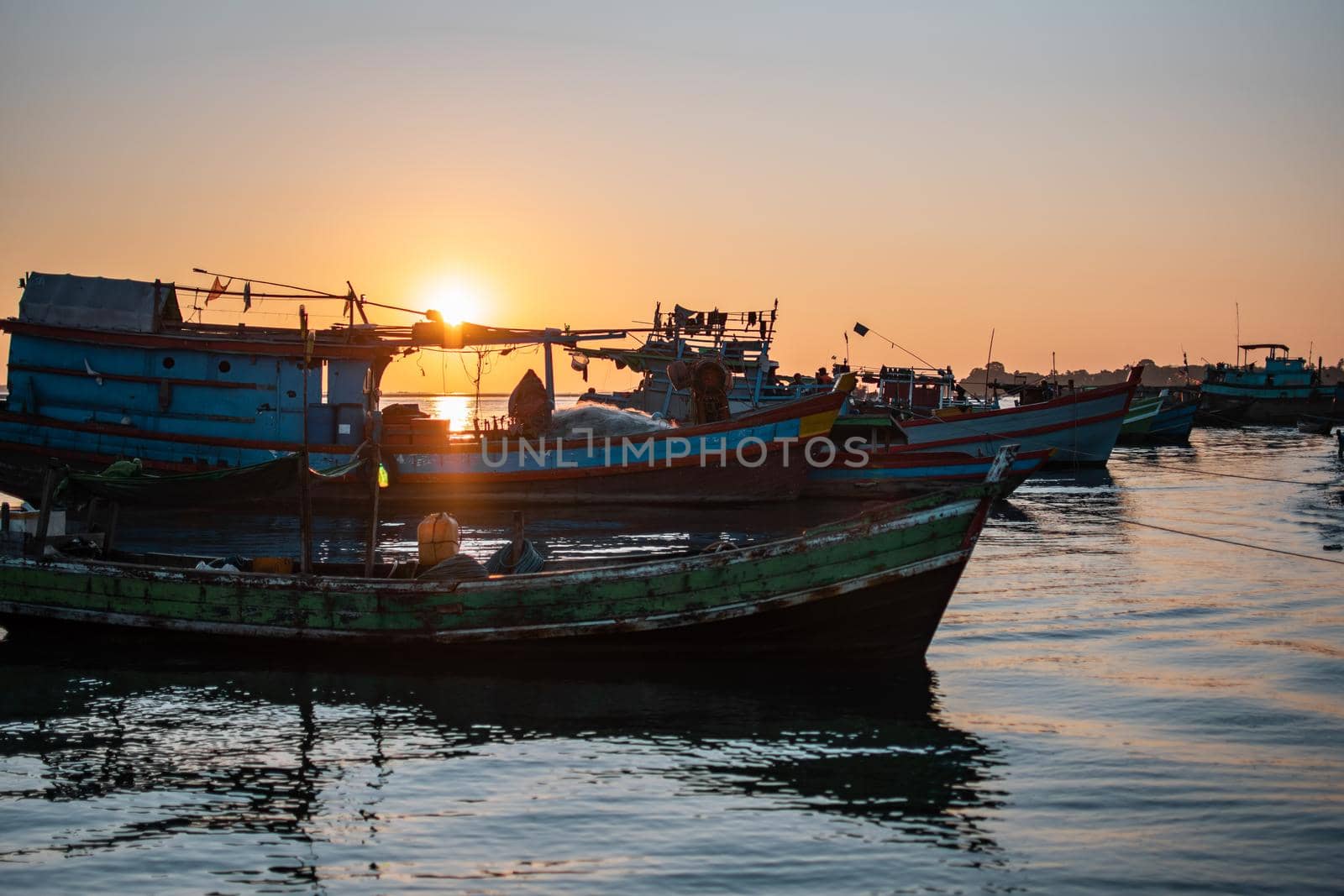 A orange beautiful sunset over colorful traditional wooden boats by the fishing society village Chaung Thar, Irrawaddy, western, Myanmar