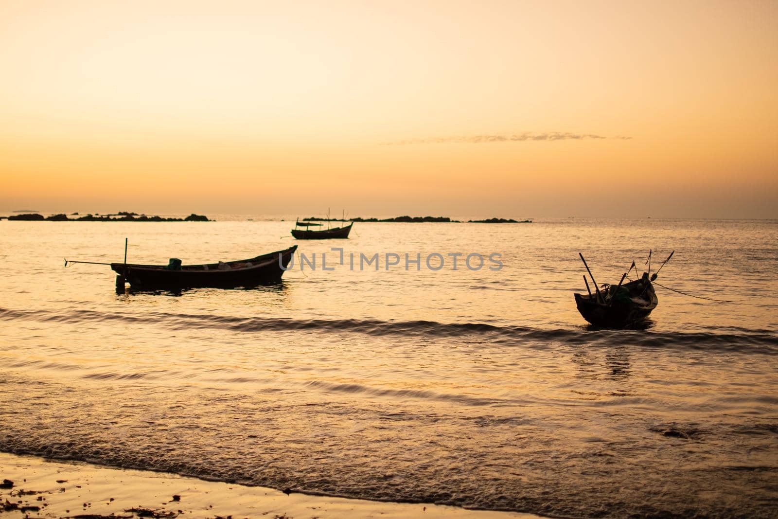 Three traditional wooden boats by the shore during a bright beautiful sunset close to Ngwesaung beach, Irrawaddy, western Myanmar