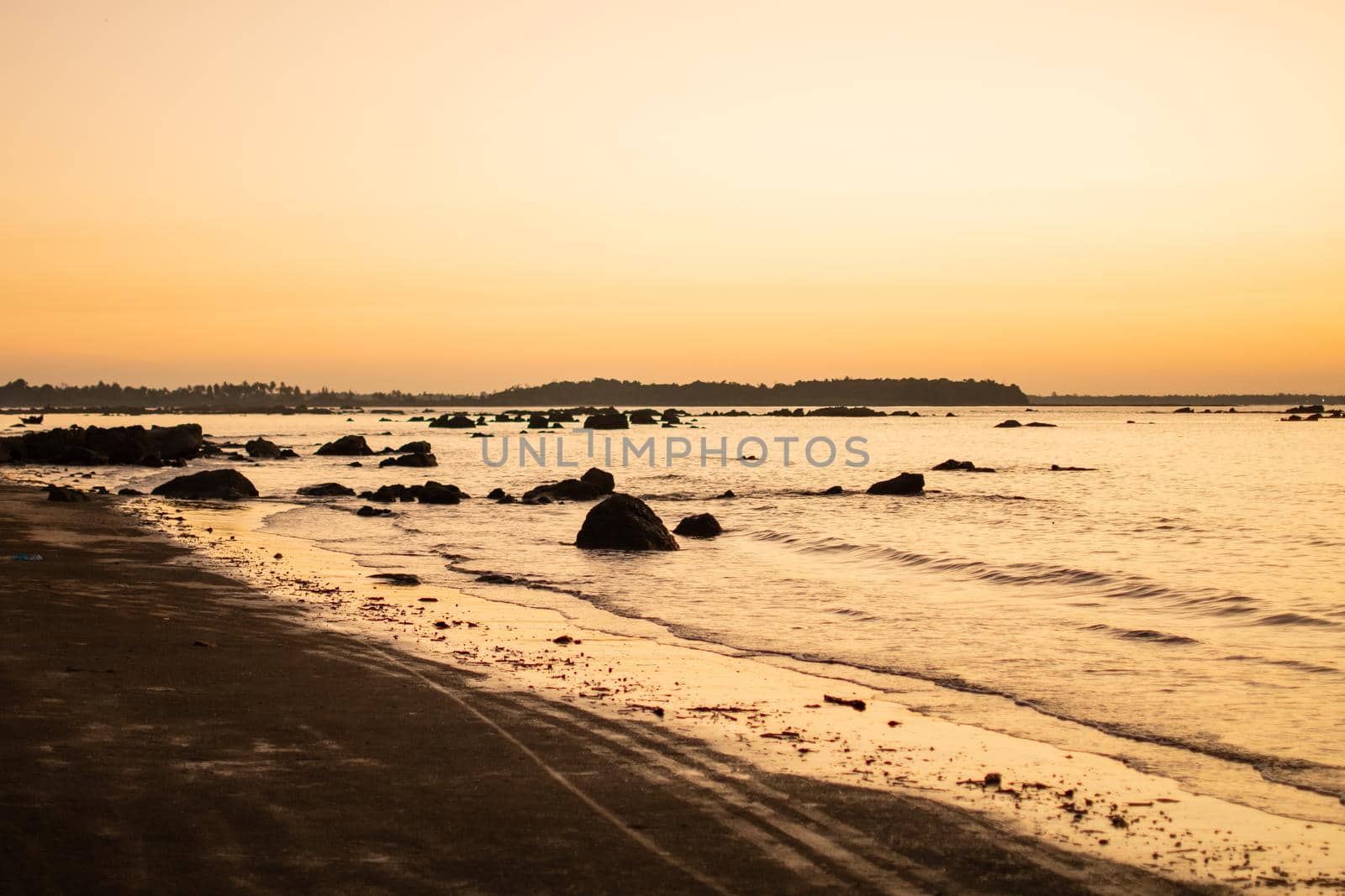 A bright golden orange sunset over a beach with rocks in the water waves near Ngwesaung beach, Irrawaddy, western Myanmar