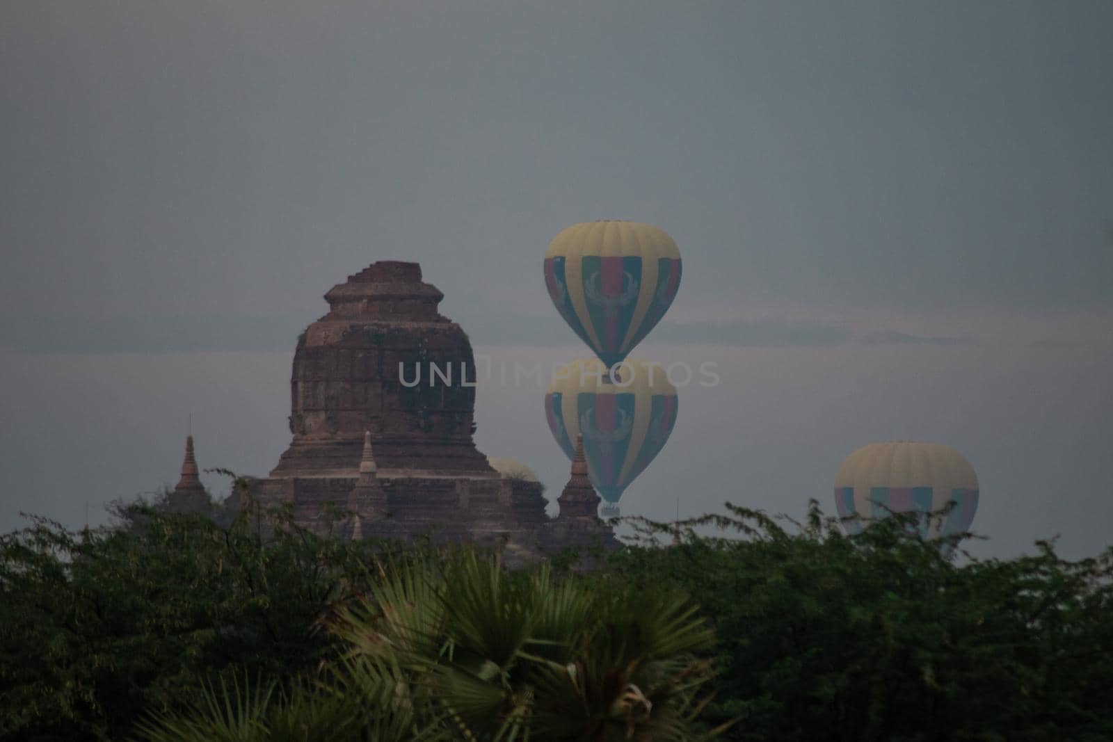 BAGAN, NYAUNG-U, MYANMAR - 2 JANUARY 2020: A few hot air balloons rises behind a historic pagoda temple