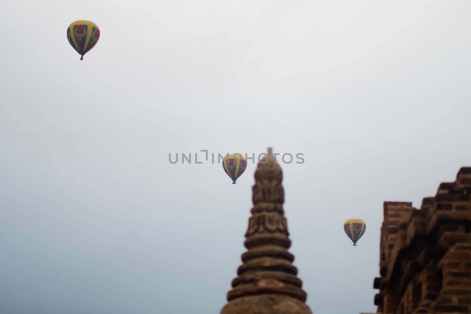 BAGAN, NYAUNG-U, MYANMAR - 2 JANUARY 2020: A few yellow, green, red and blue multicolored hot air balloon in the sky above a historic temple