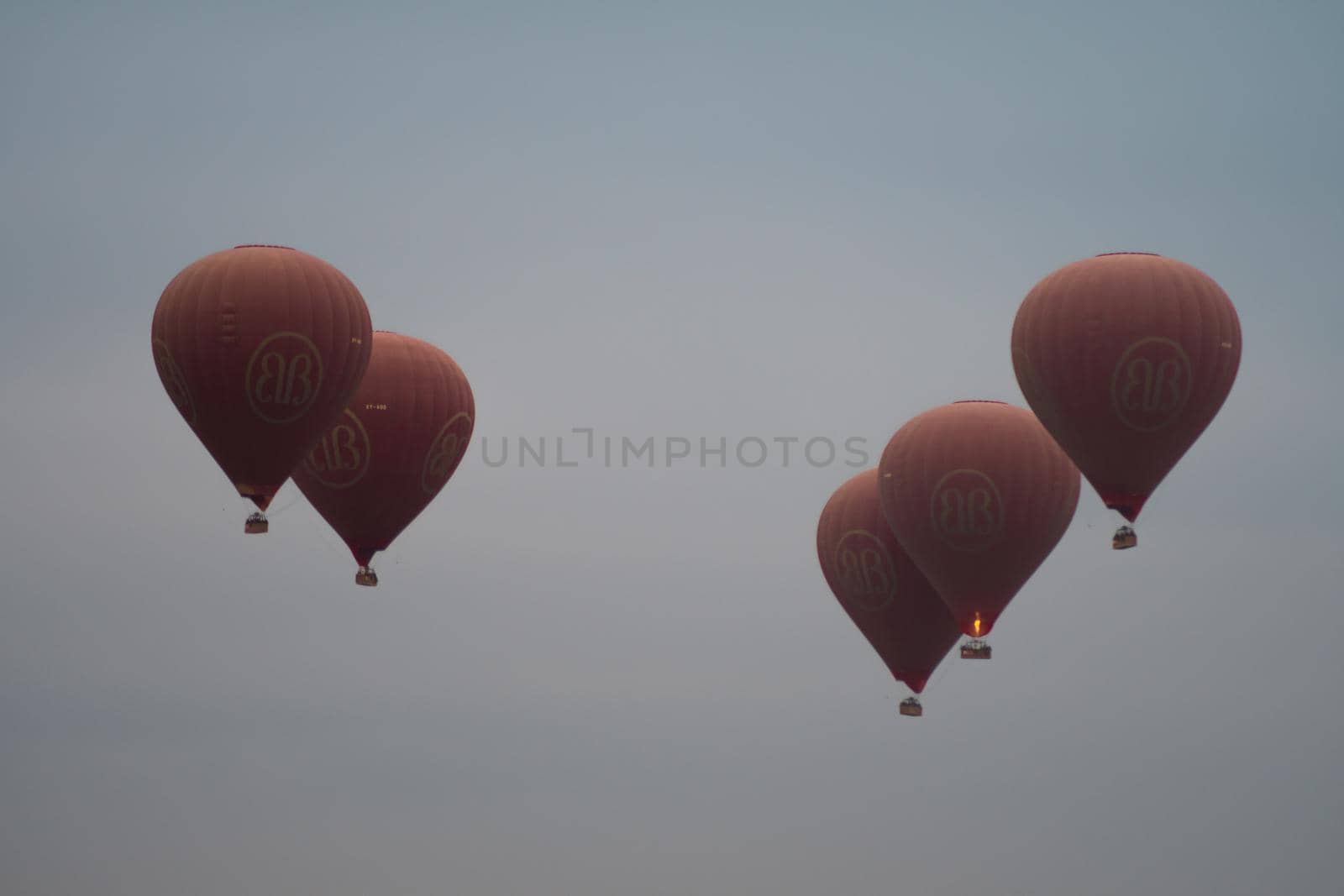 BAGAN, NYAUNG-U, MYANMAR - 2 JANUARY 2020: Five red hot air balloons rises high in the sky together for tourists
