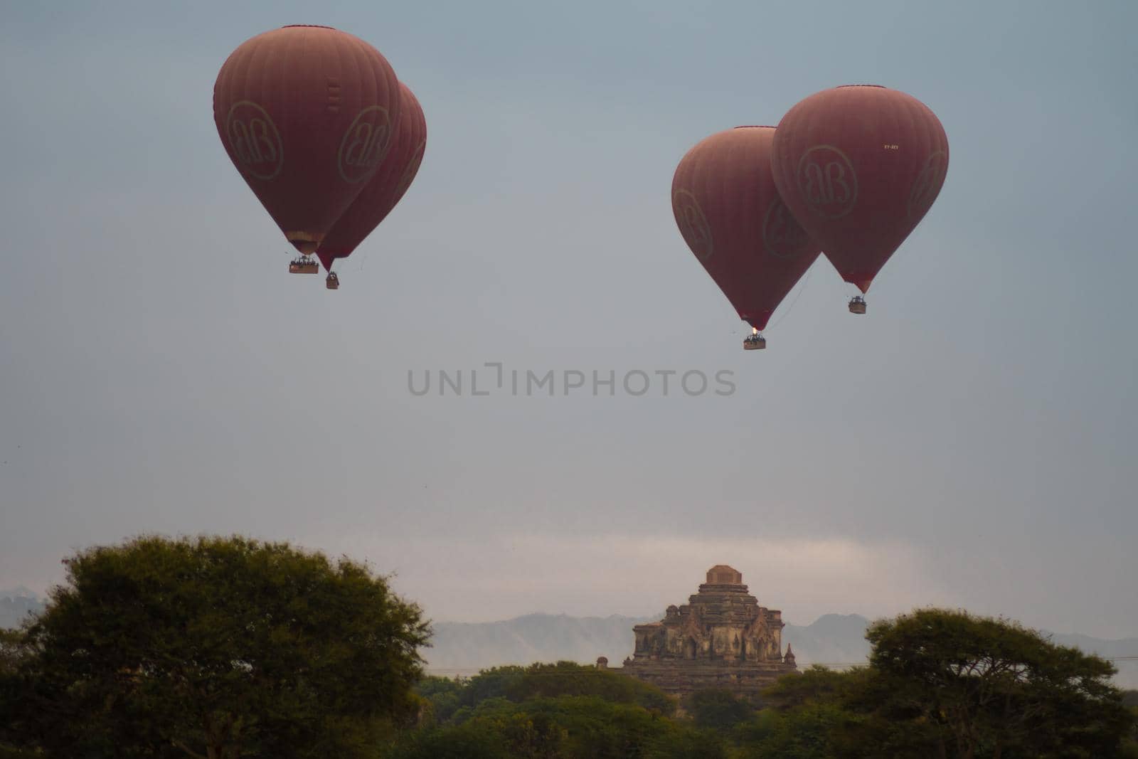 BAGAN, NYAUNG-U, MYANMAR - 2 JANUARY 2020: A few hot air balloons rises above a historic pagoda temple in the distance