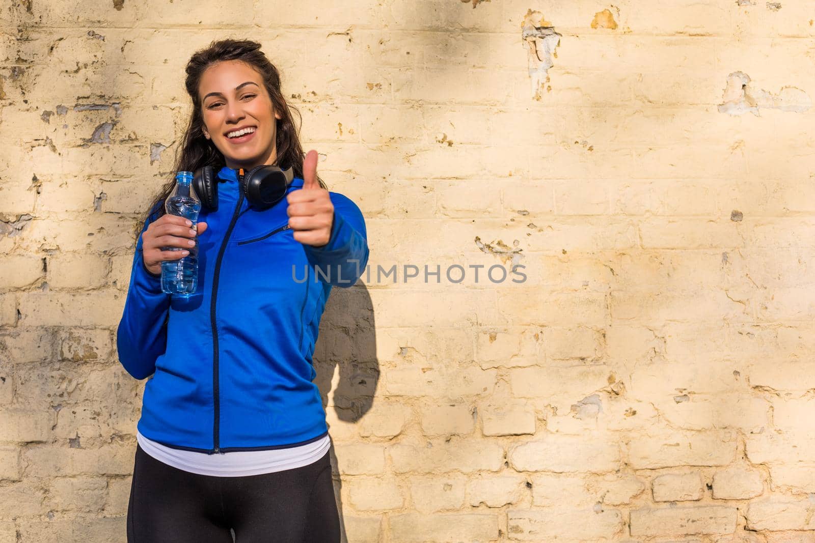 Beautiful sporty  woman drinking water outdoor and showing thumb up.