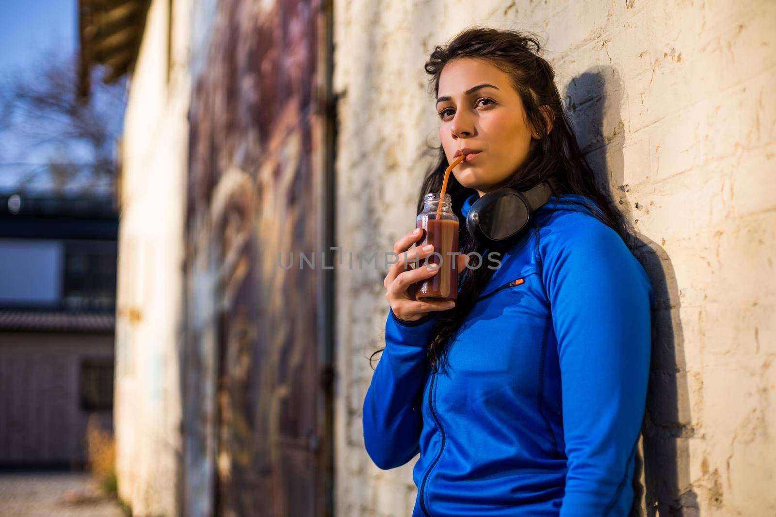 Beautiful sporty woman enjoys drinking smoothie outdoor.
