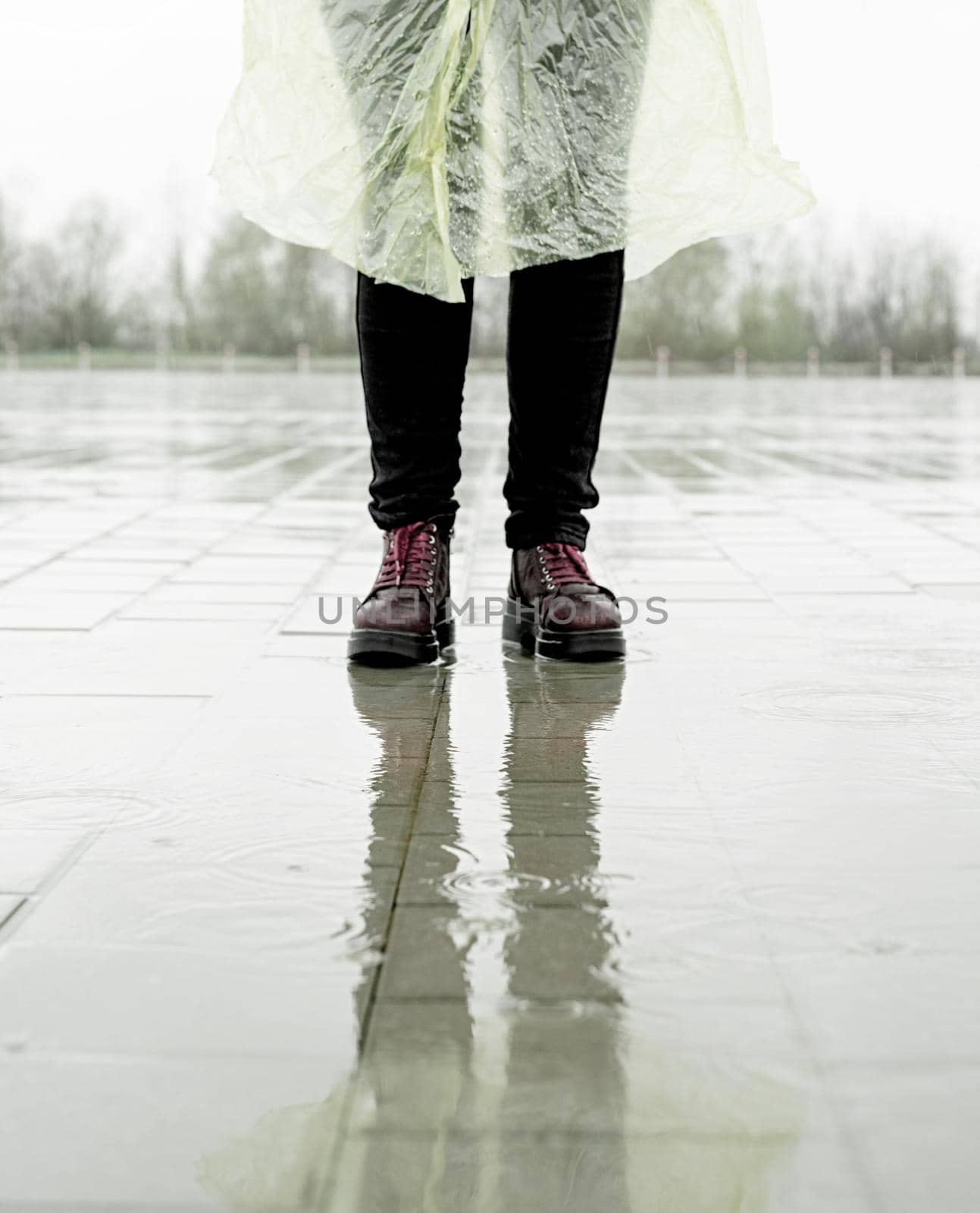 woman walking on asphalt in rainy weather. Close up of legs and shoes standing in puddles