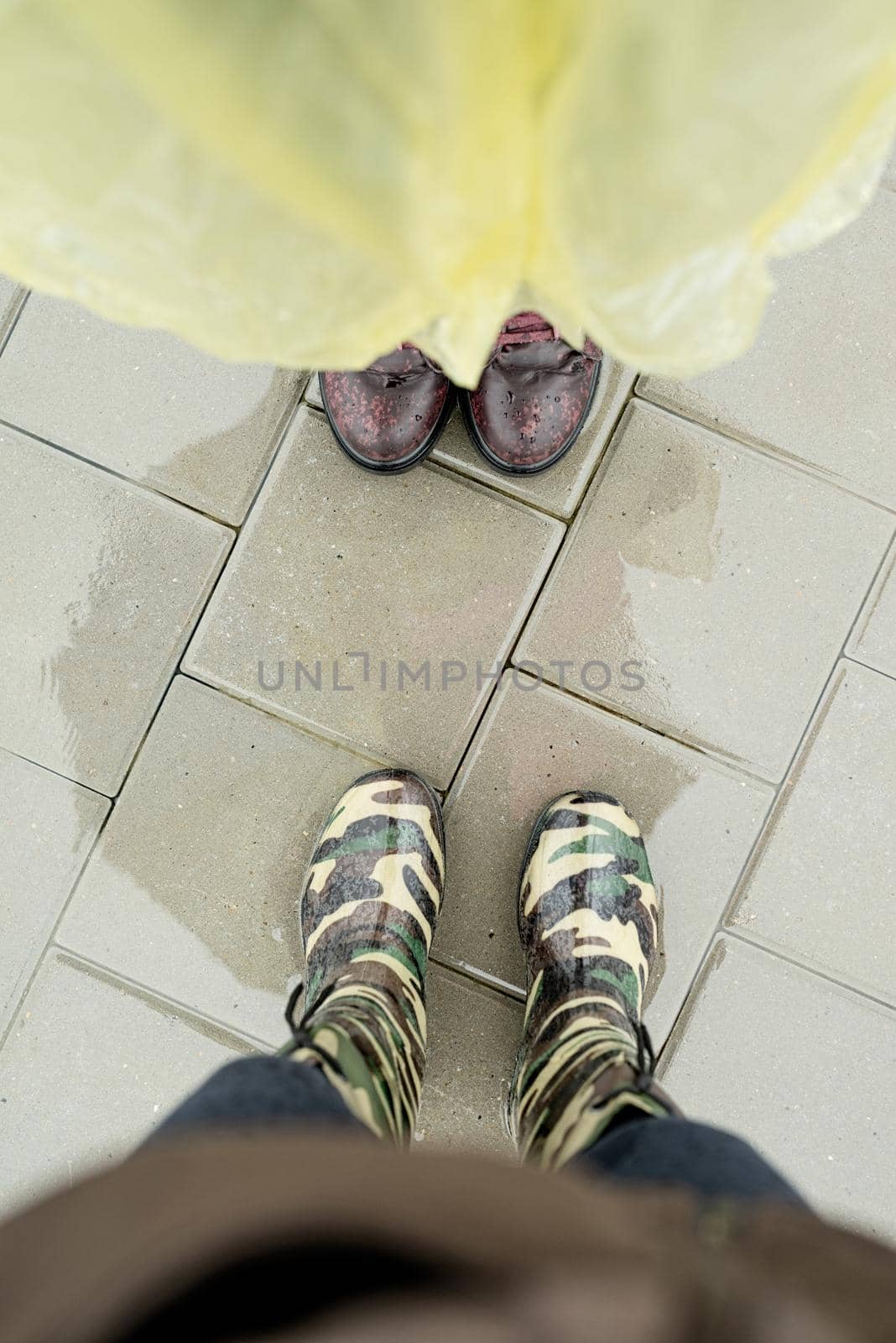 Top view of two pairs of female feet standing in puddles in rainy day, looking towards each other