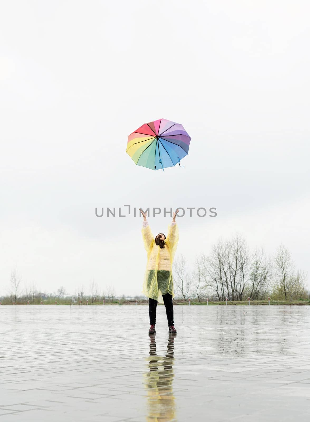 brunette woman throwing colorful umbrella up in the rain by Desperada