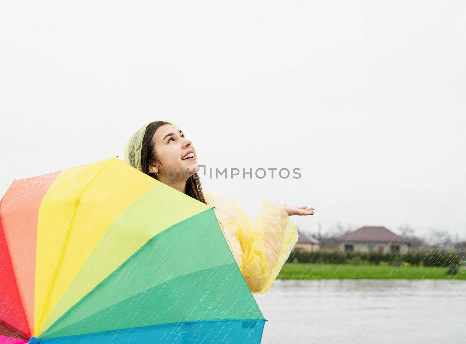 Beautiful brunette woman holding colorful umbrella out in the rain by Desperada