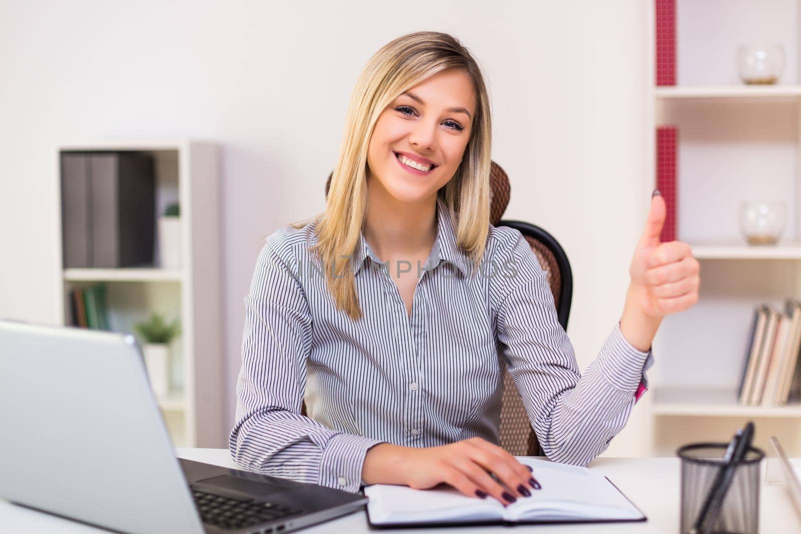 Businesswoman showing thumb up while  working by Bazdar