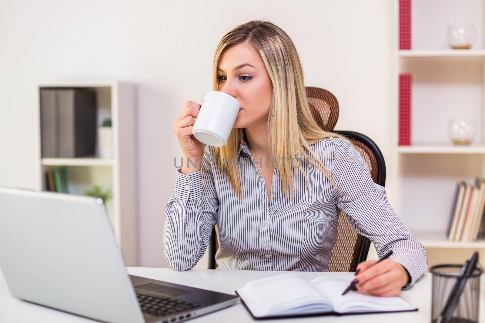 Businesswoman drinking coffee while working in her office.