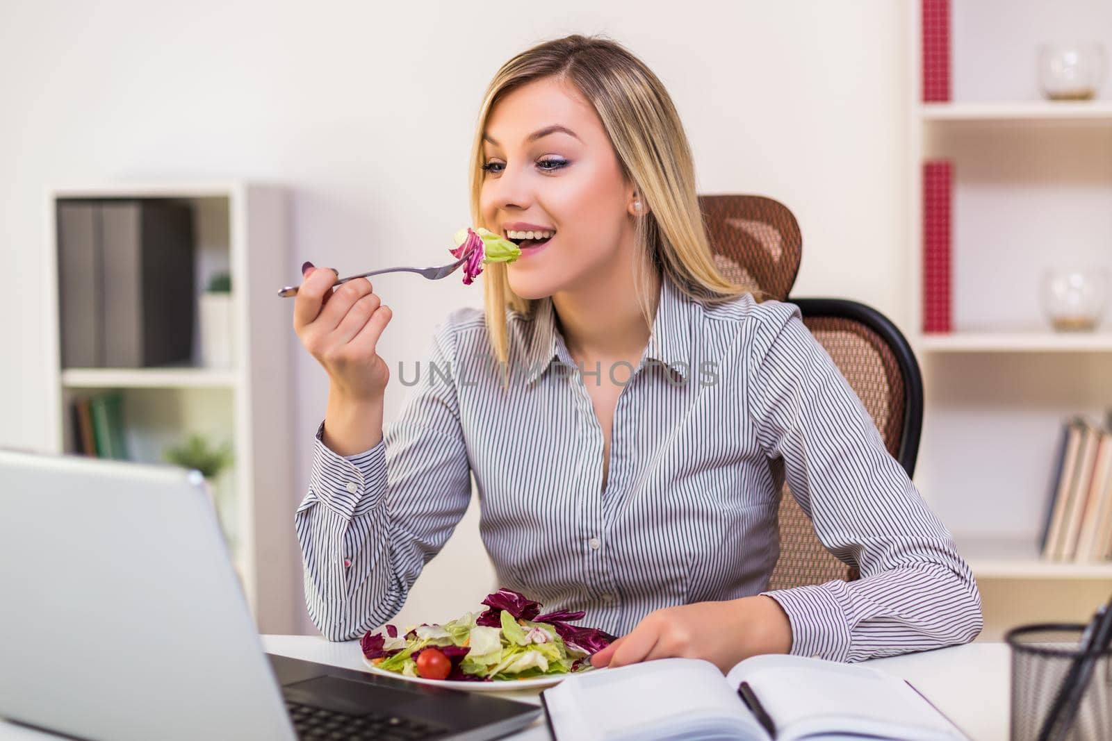 Businesswoman eating salad while working by Bazdar