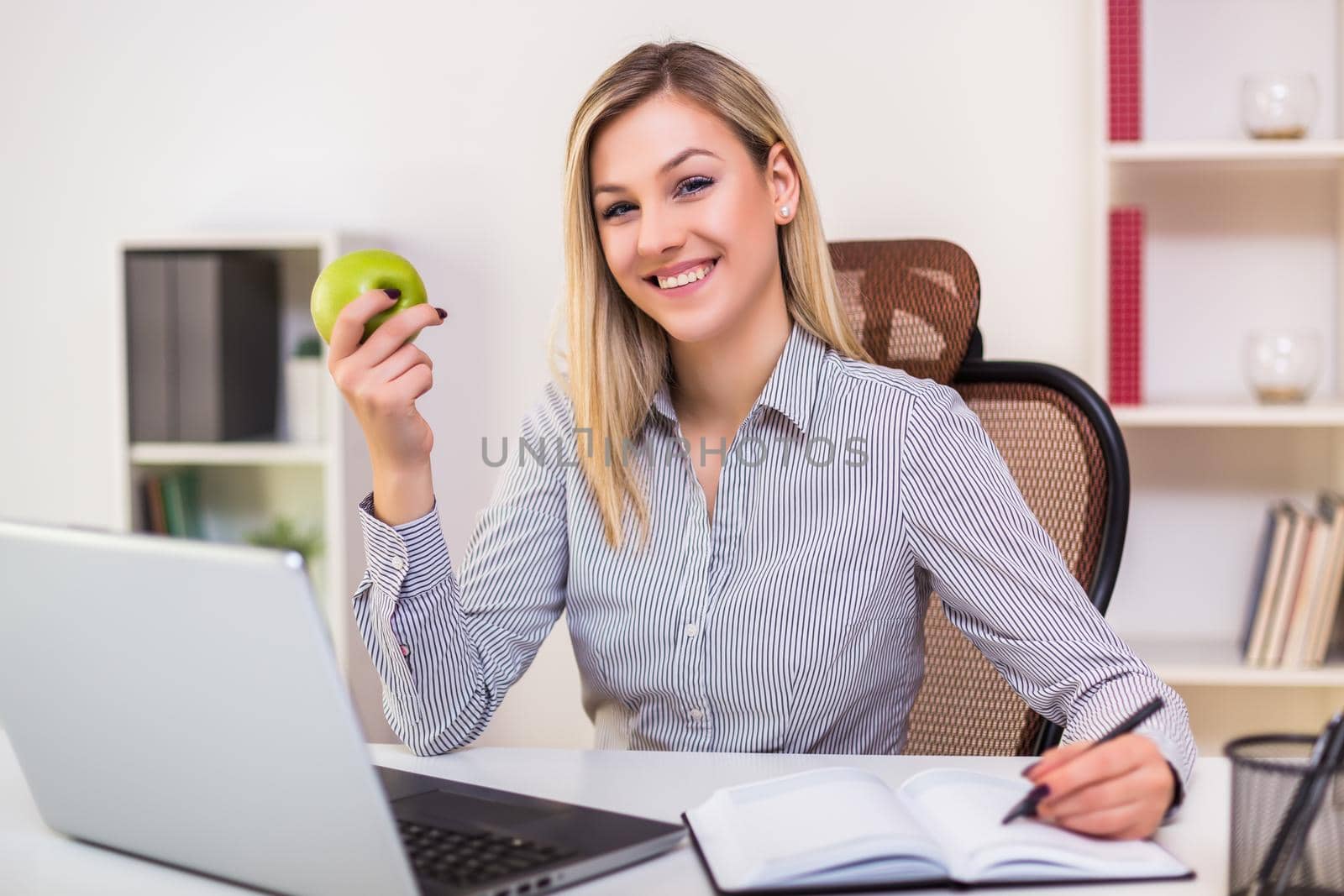 Businesswoman eating apple while working by Bazdar