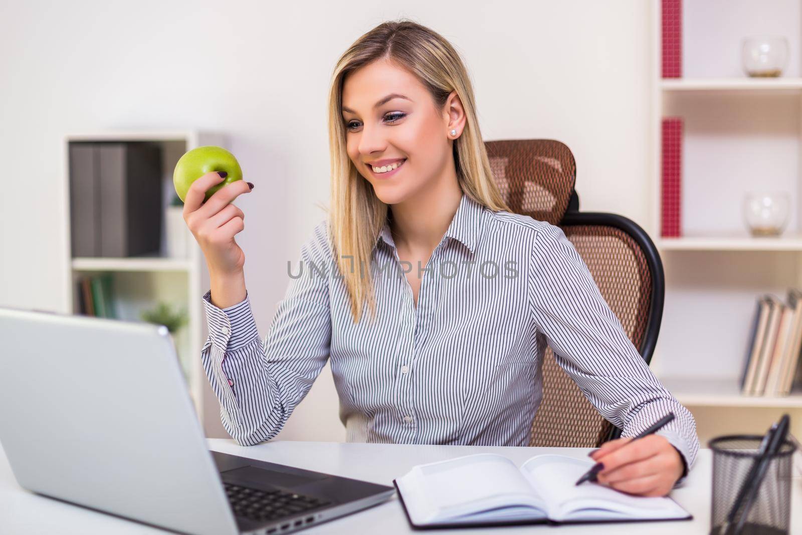 Businesswoman eating apple while working in her office.