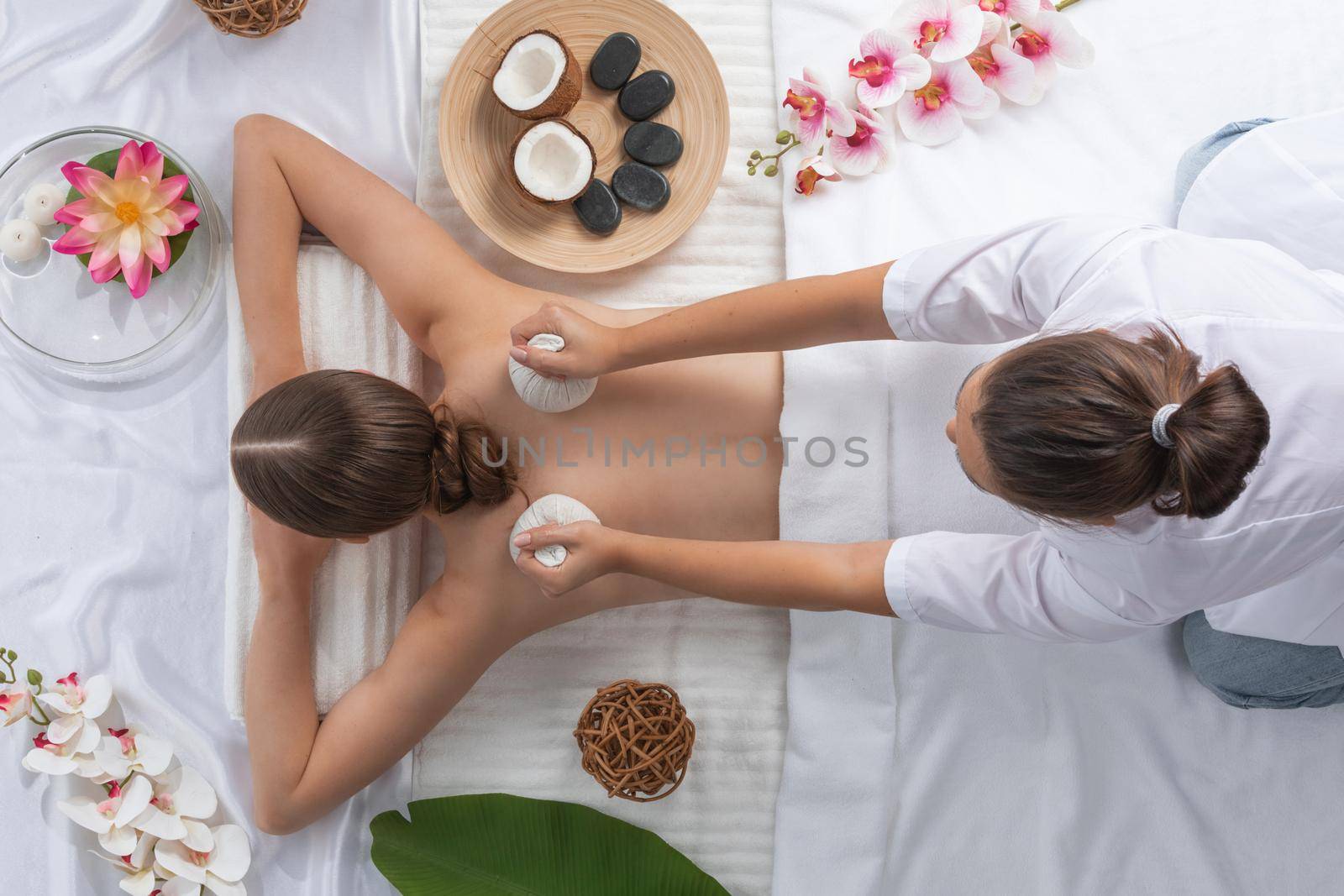 Woman at spa thai massage tow view, beauty treatments concept. Orchid and lotus flowers coconut stones and herb pouches